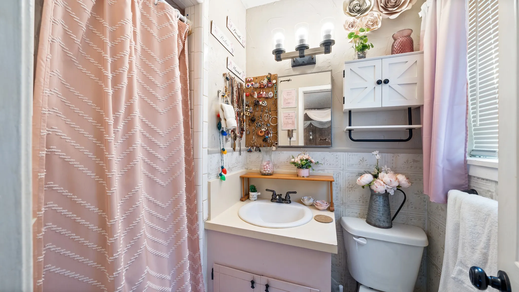 White vanity with a single basin sink, wall-mounted light fixture, and a wall-mounted storage cabinet
