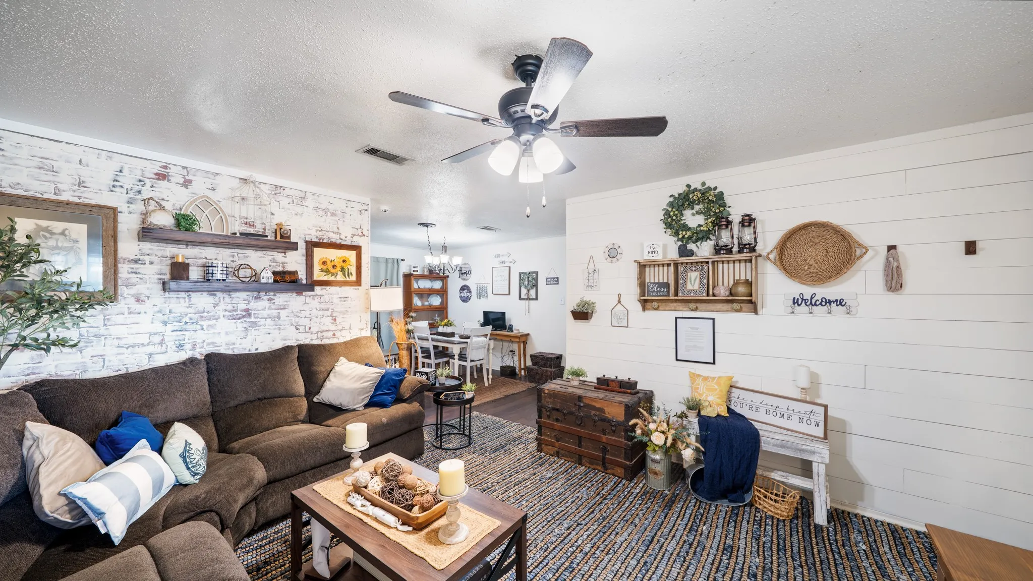 Distressed brick-finish accent wall, wood-finish ceiling fan with integrated lighting, and white shiplap-style wall paneling