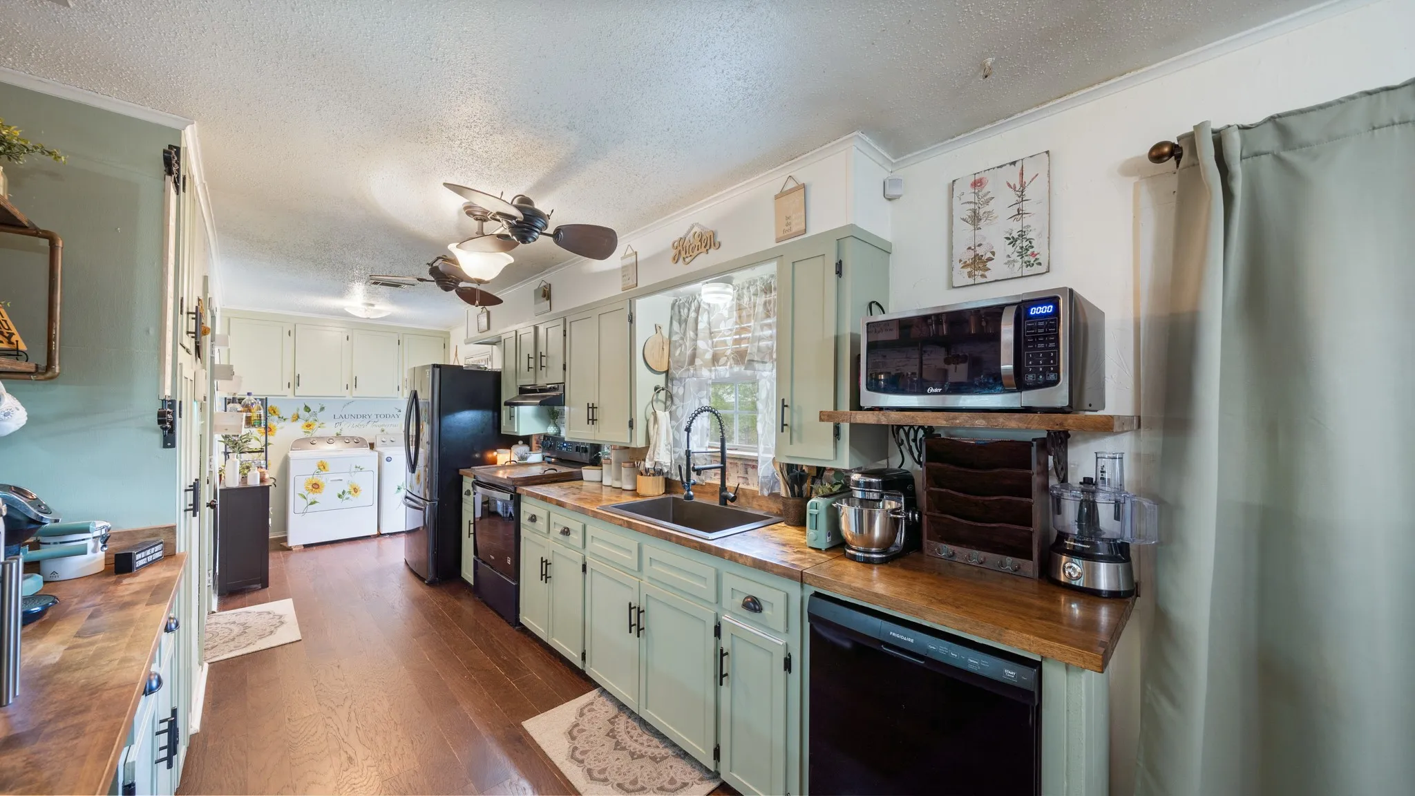 Wood-finish flooring, light green cabinetry, black appliances, wood-finish countertops, and ceiling fans
