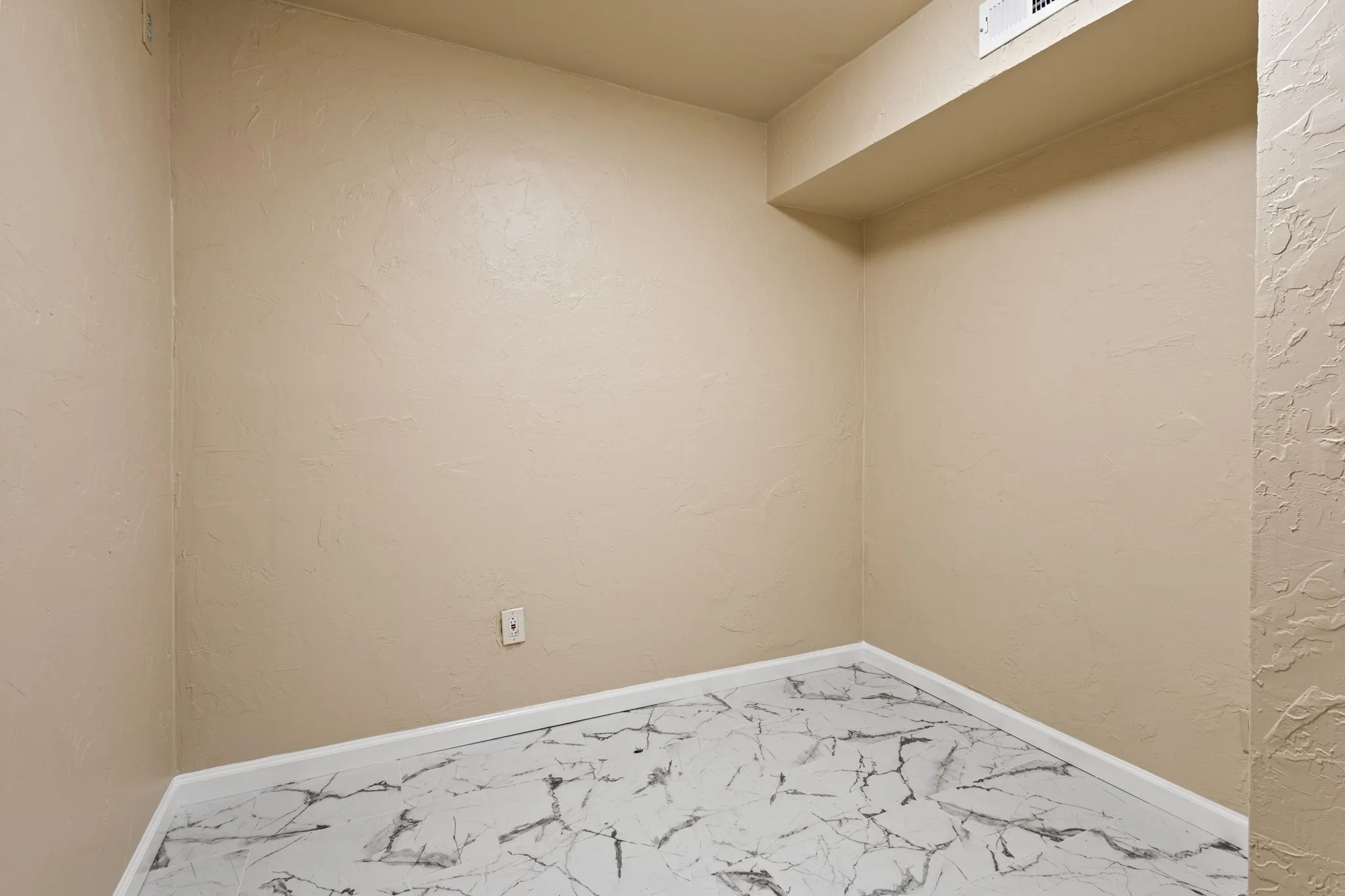 Empty room featuring marble finish floors and a textured wall
