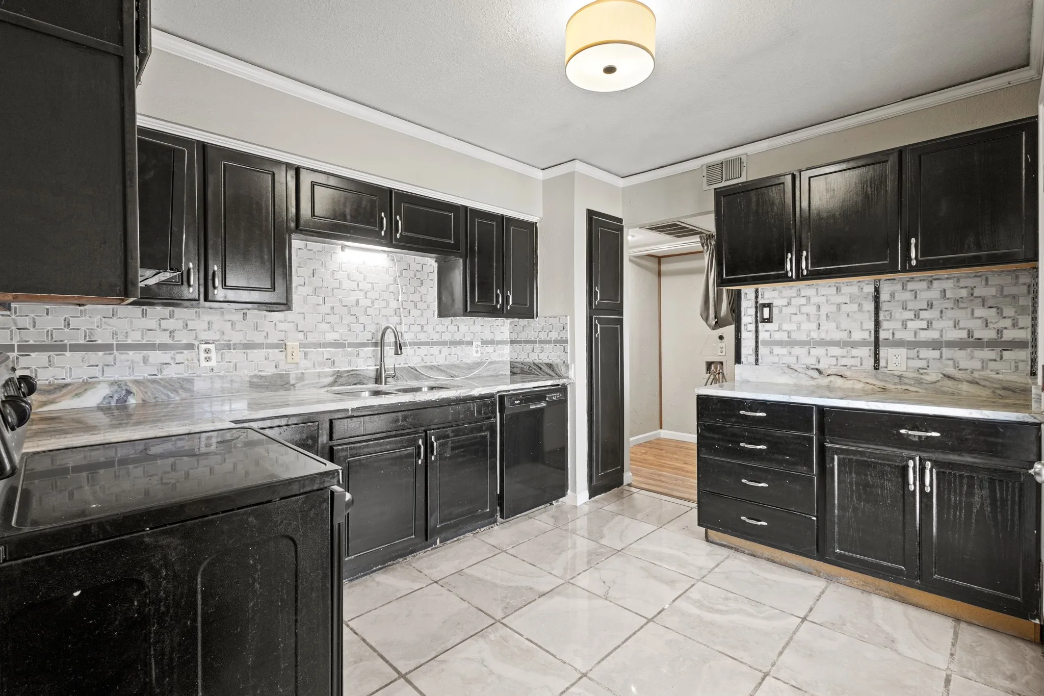 Kitchen with dark cabinetry, decorative backsplash, black appliances, ornamental molding, and light stone counters