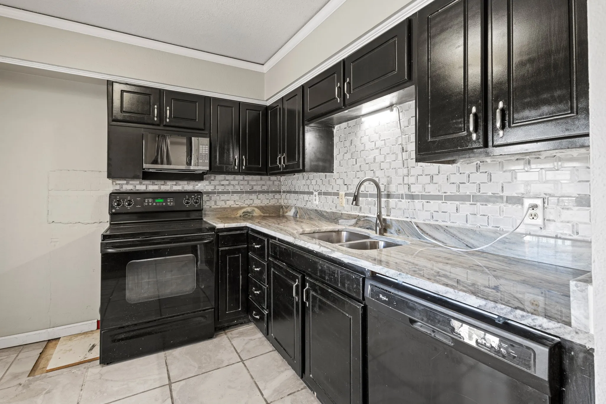 Kitchen with dark cabinets, black appliances, ornamental molding, backsplash, and light stone countertops