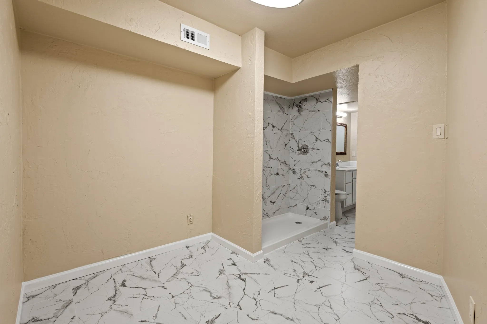 Full bathroom with marble finish floors, a shower stall, and a textured wall