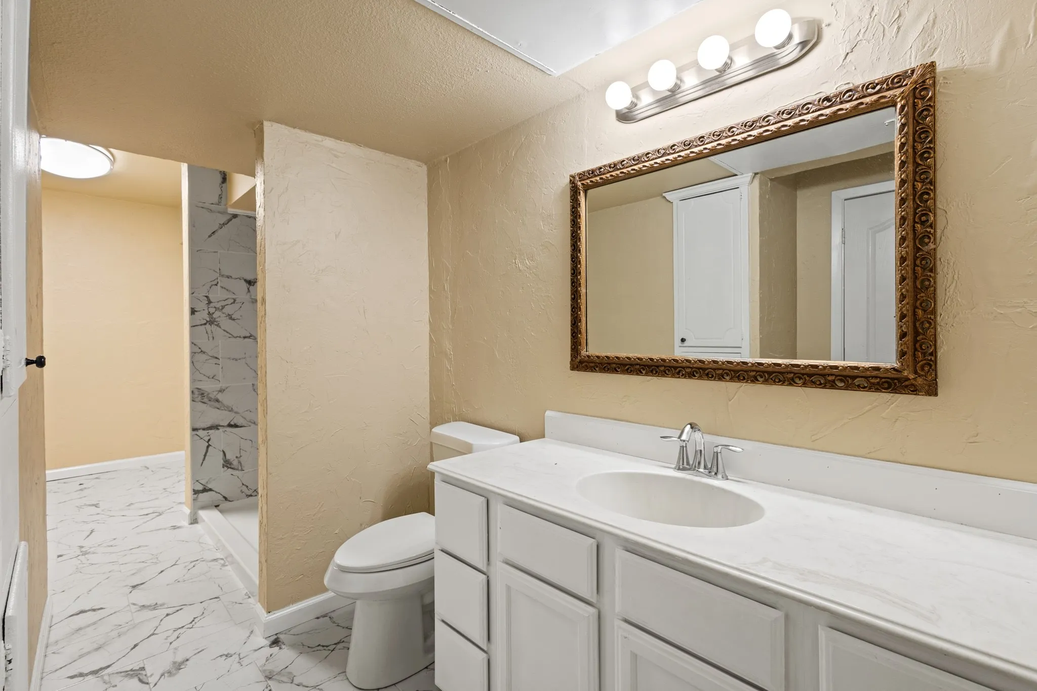 Full bathroom with marble finish floors, a textured wall, vanity, a stall shower, and a textured ceiling