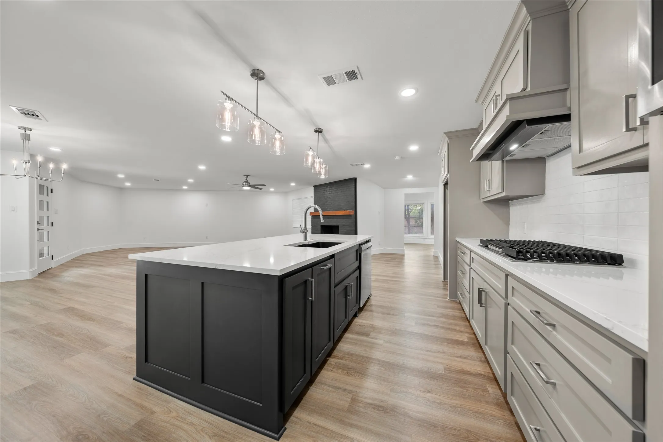 Kitchen featuring open floor plan, light wood-type flooring, a kitchen island with sink, a ceiling fan, and decorative light fixtures