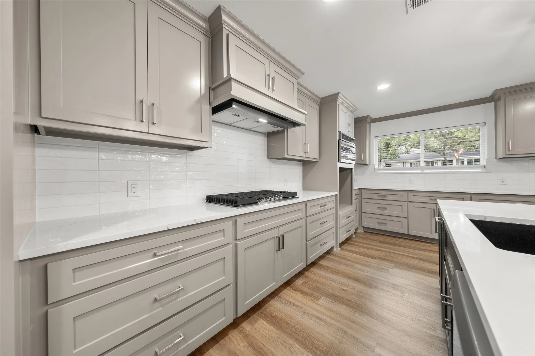 Kitchen with gray cabinetry, crown molding, backsplash, light wood-style flooring, and light stone countertops
