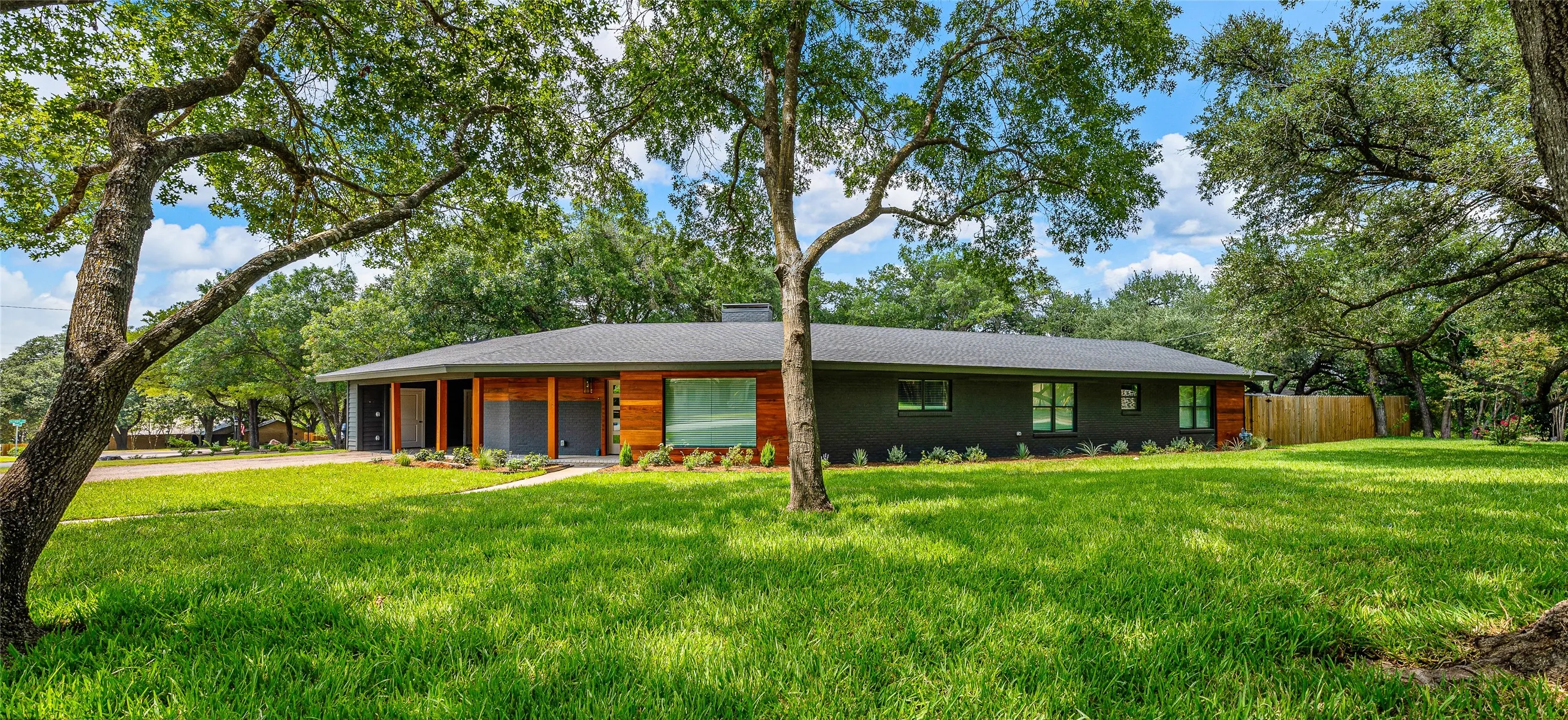 Single story home featuring a chimney, driveway, roof with shingles, and view of scattered trees