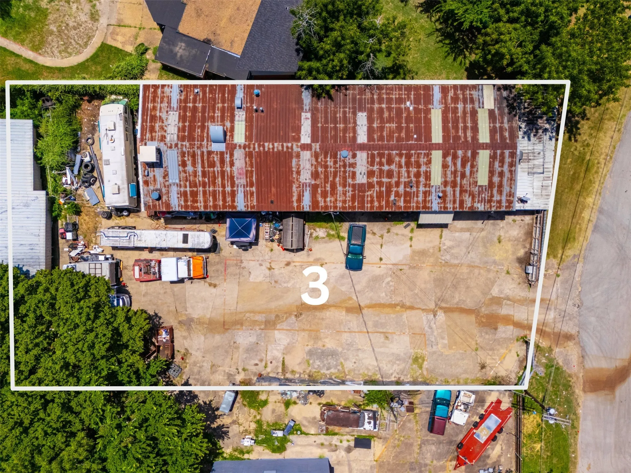 Expansive paved lot with substantial industrial building featuring a corrugated metal roof