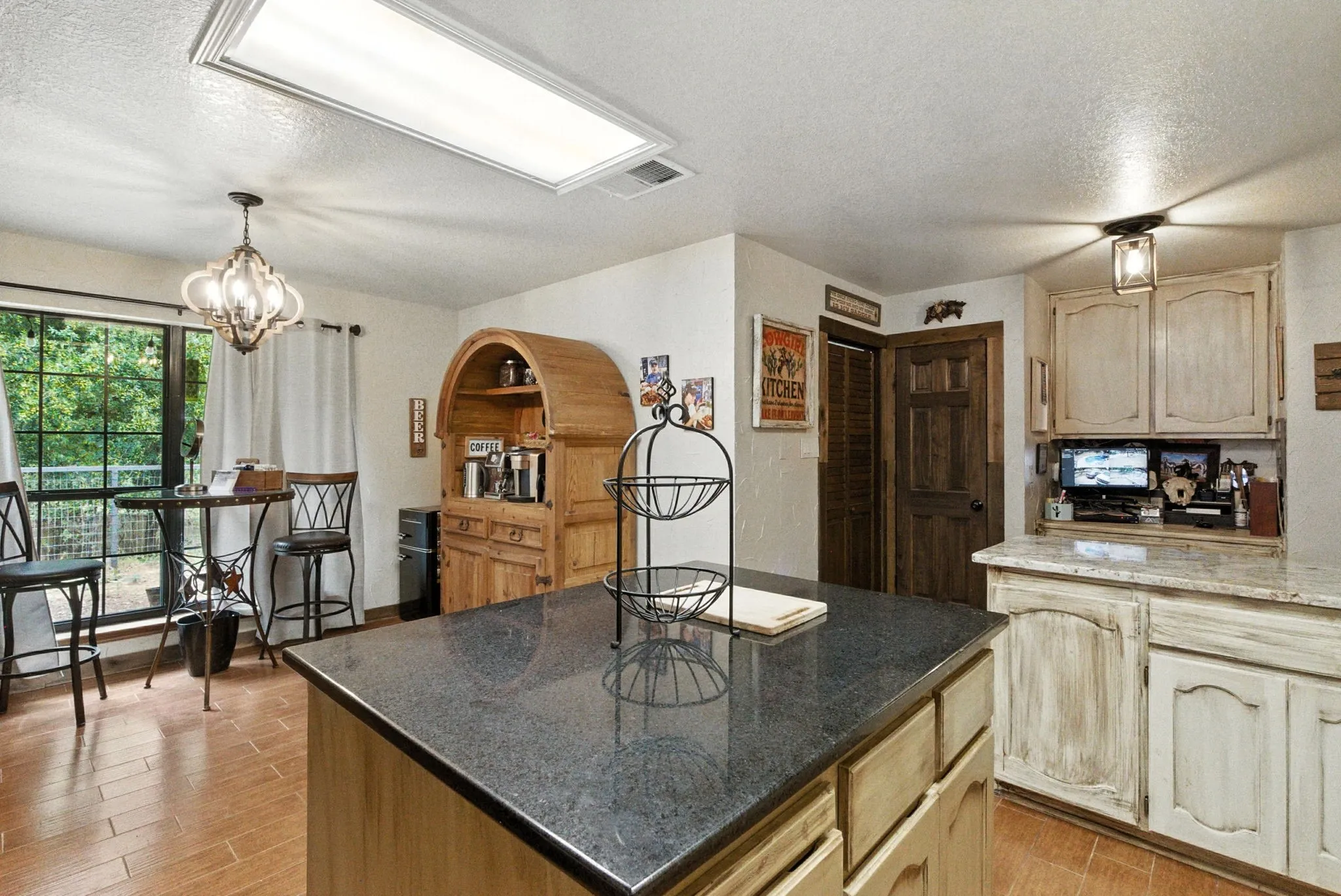 Kitchen with a textured ceiling, light wood-style floors, a chandelier, decorative light fixtures, and a kitchen island