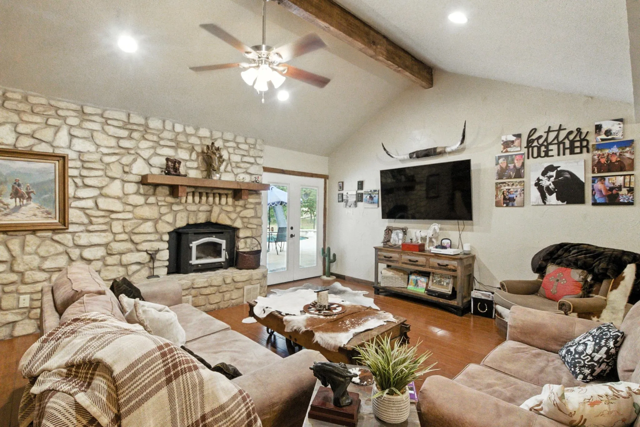 Living room featuring wood finished floors, beamed ceiling, french doors, ceiling fan, and a wood stove