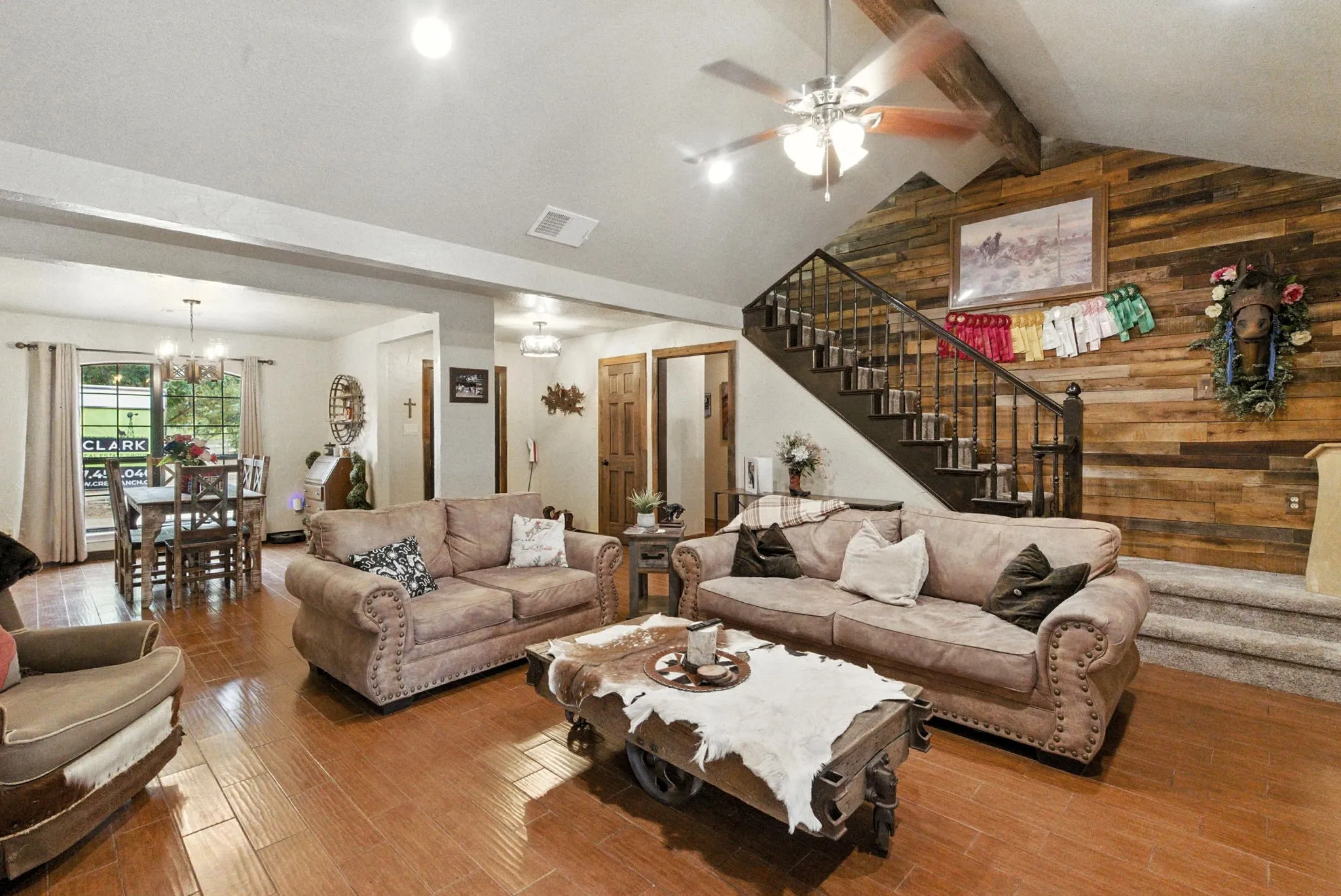 Living room featuring stairway, wood walls, wood finished floors, a chandelier, and a ceiling fan