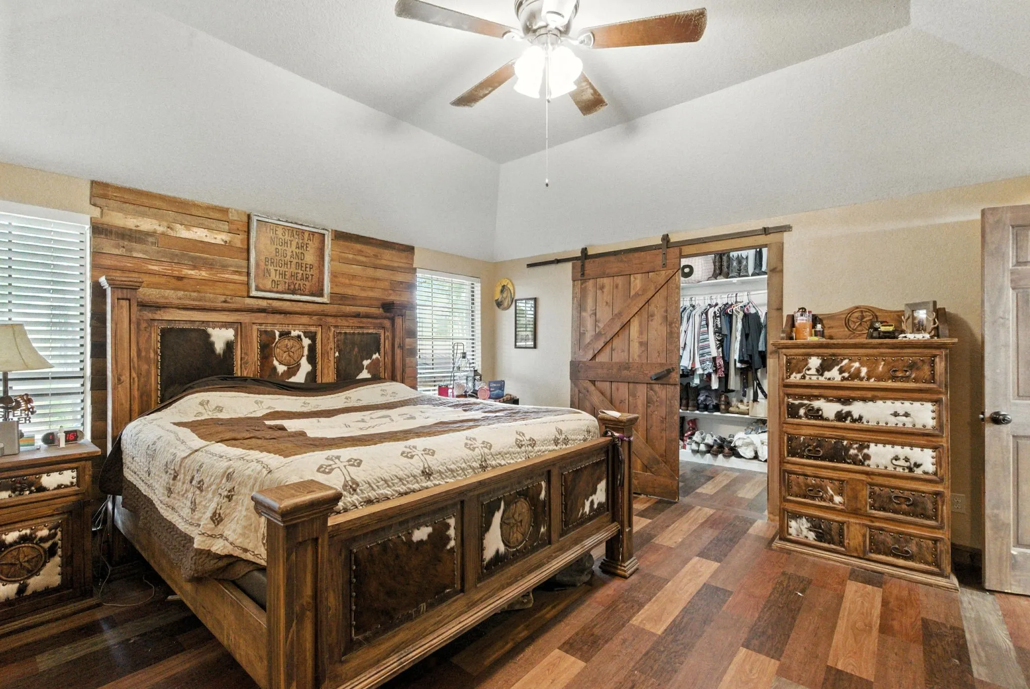 Bedroom with lofted ceiling, a barn door, wood finished floors, a walk in closet, and a ceiling fan