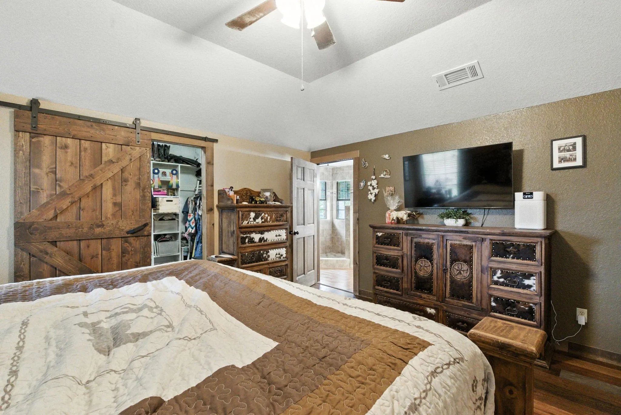 Bedroom with lofted ceiling, wood finished floors, a barn door, ensuite bathroom, and a walk in closet