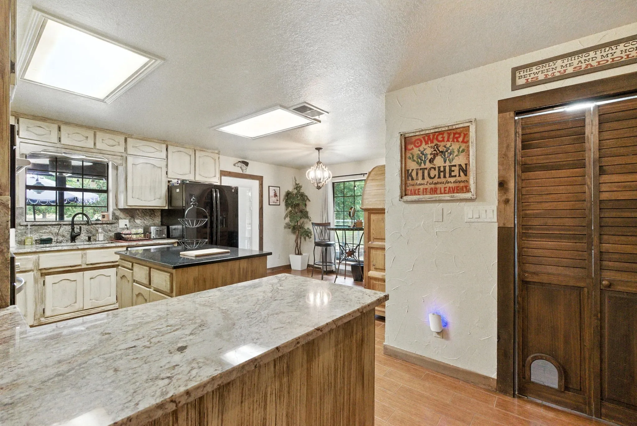 Kitchen featuring a textured ceiling, healthy amount of natural light, light wood-type flooring, a textured wall, and a chandelier