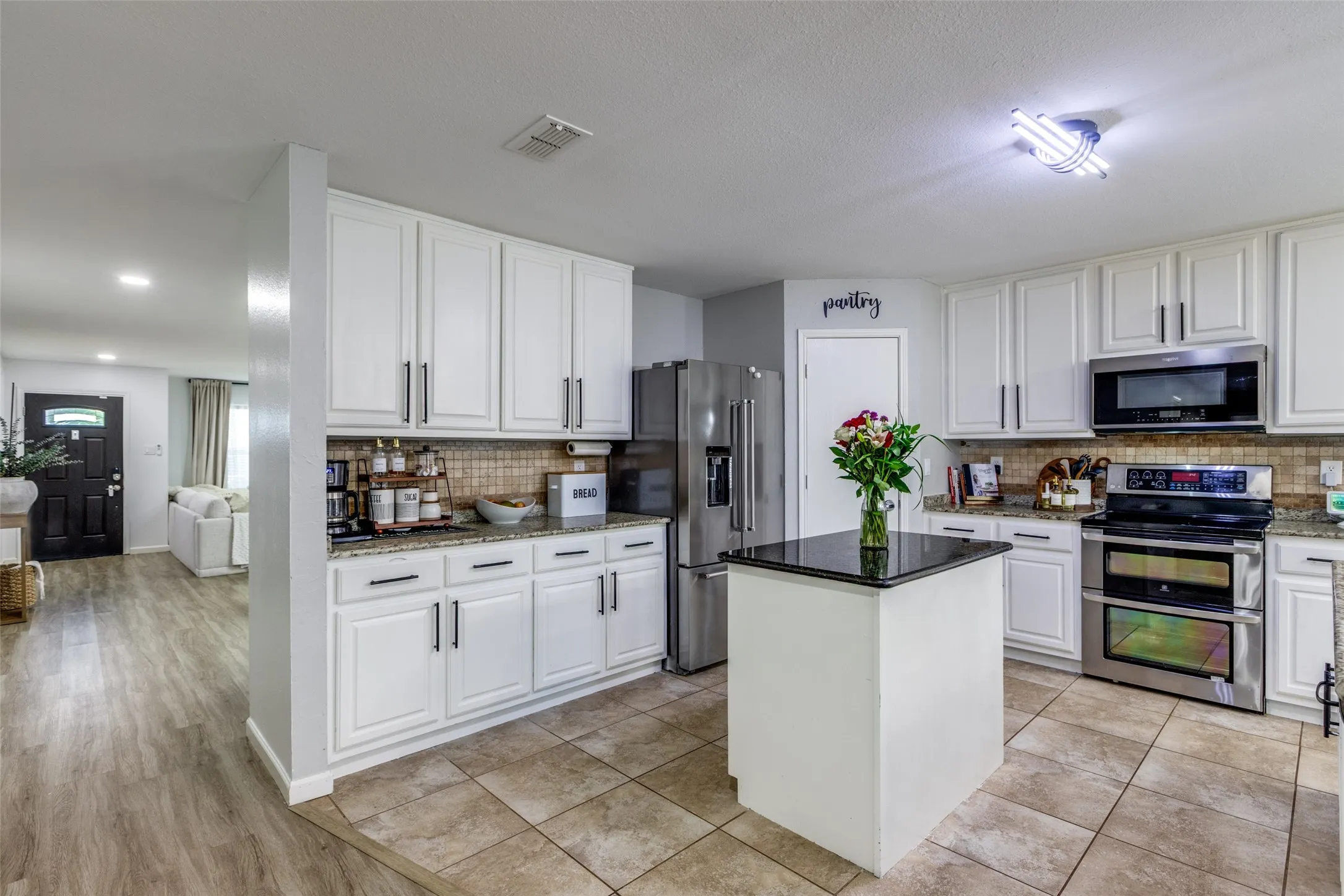 Kitchen featuring appliances with stainless steel finishes, white cabinetry, tasteful backsplash, a kitchen island, and stone countertops