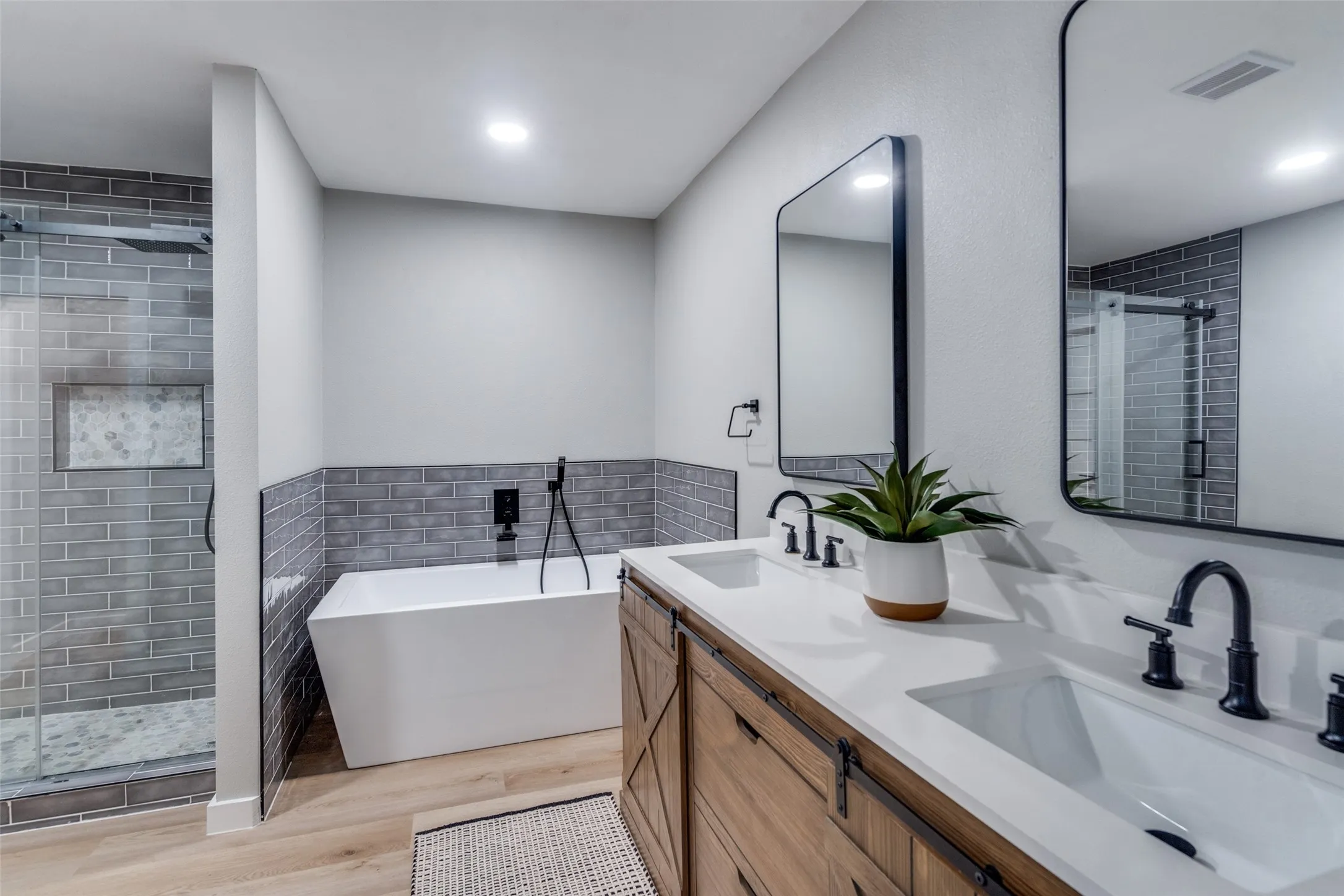 Full bath with wood finished floors, a soaking tub, double vanity, a stall shower, and tile walls