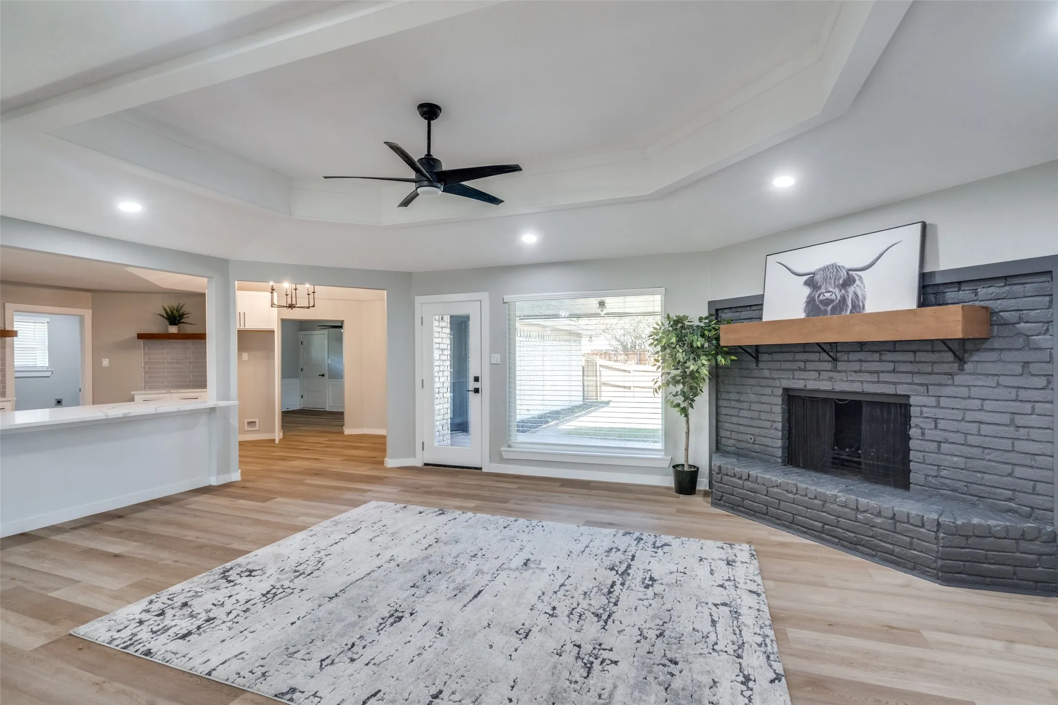 Living area with a tray ceiling, a fireplace, light wood finished floors, recessed lighting, and ceiling fan