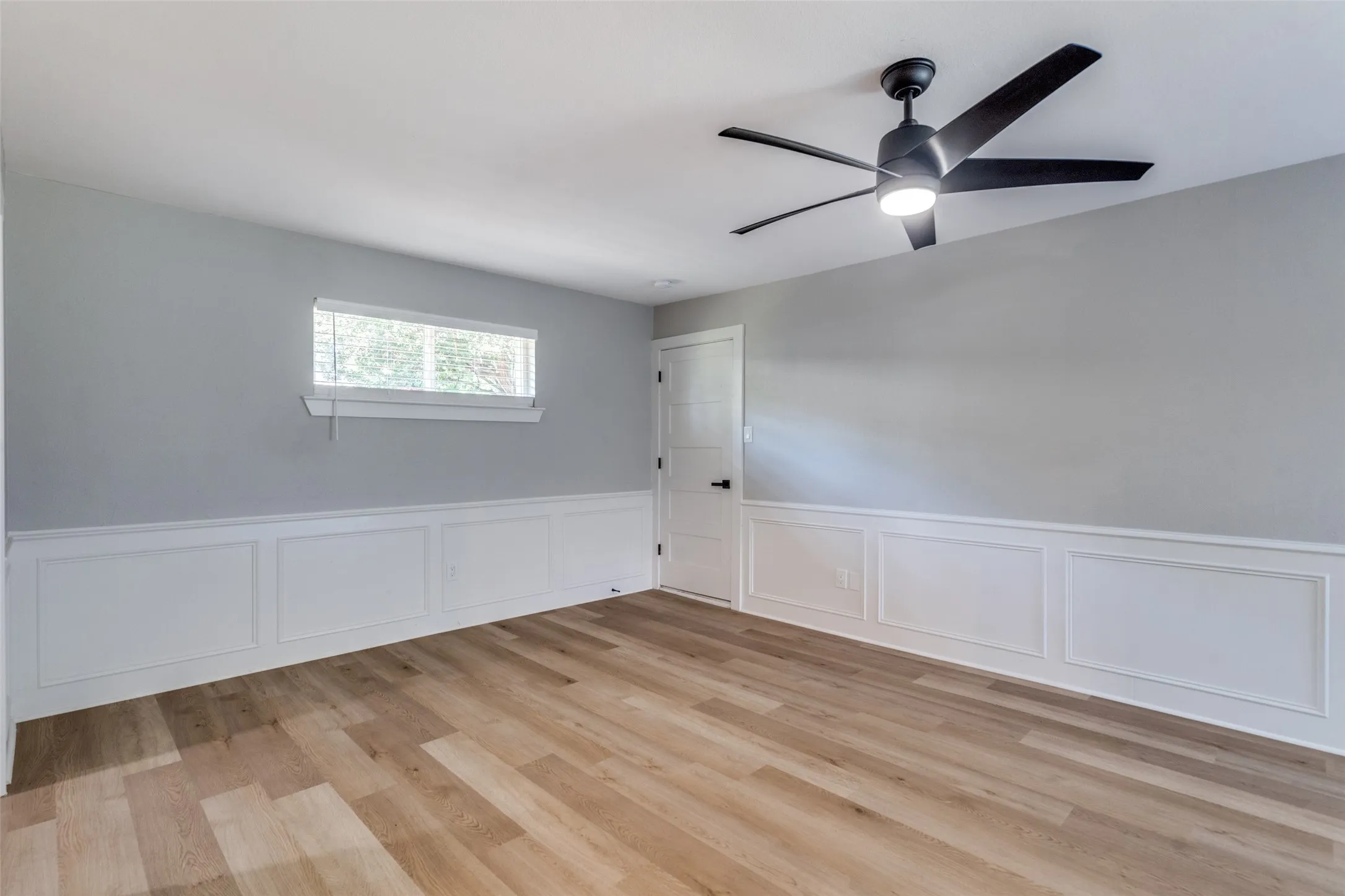 Empty room featuring light wood-style floors, wainscoting, a decorative wall, and ceiling fan