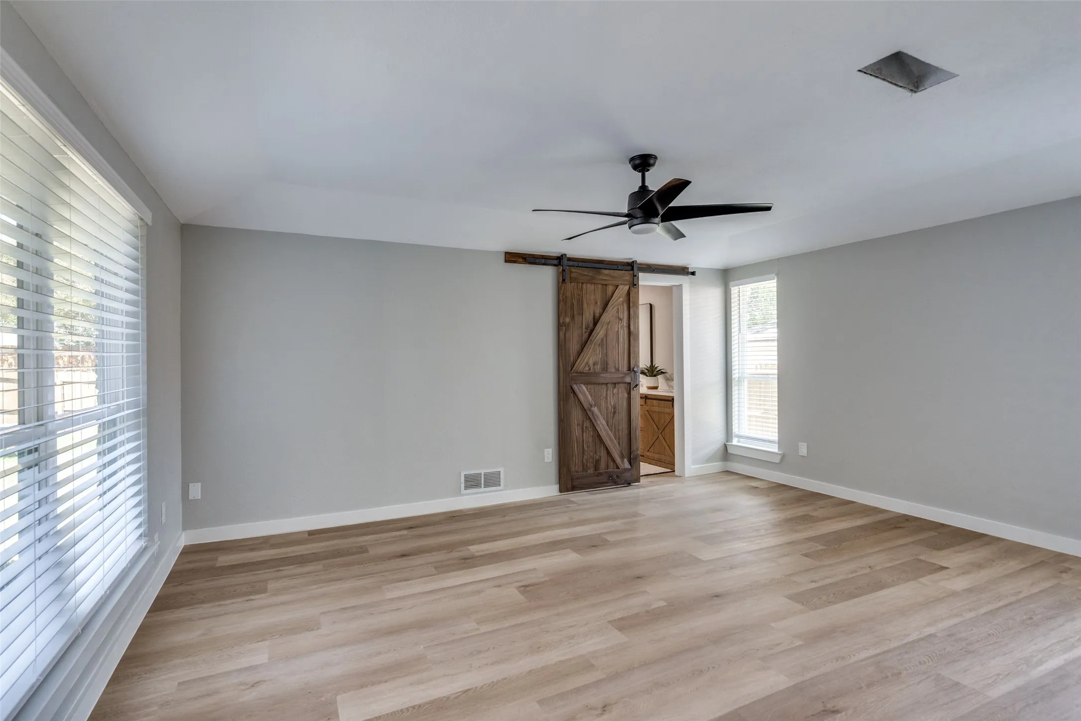Empty room with a barn door, light wood-style flooring, and a ceiling fan