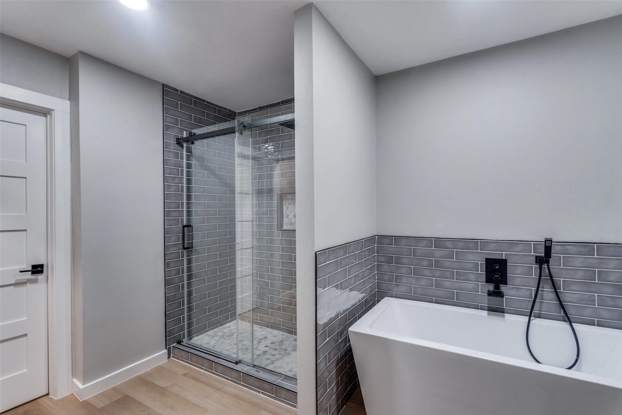 Bathroom with wood finished floors, a soaking tub, a shower stall, and tile walls