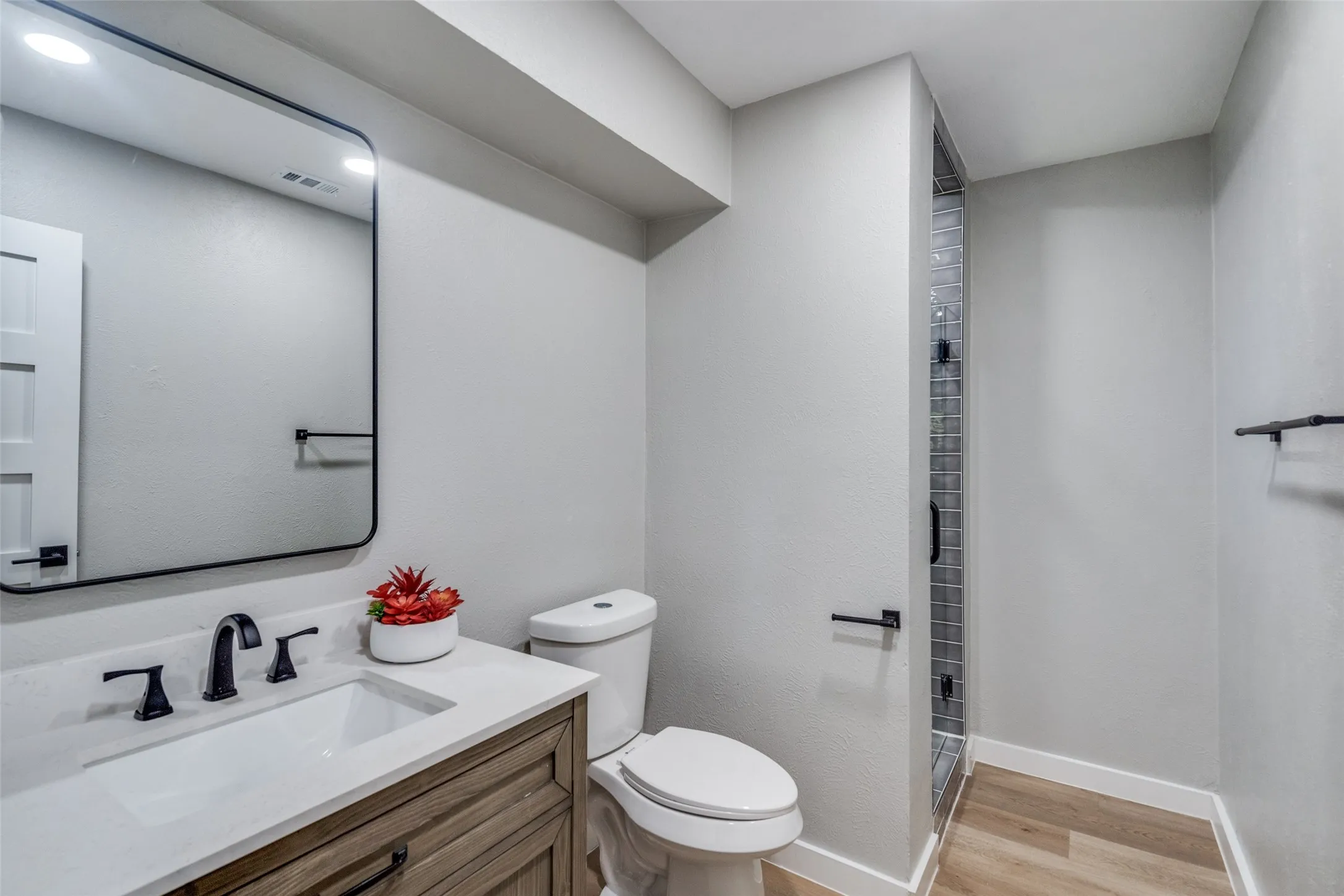 Full bath featuring wood finished floors, vanity, a shower, and a textured wall