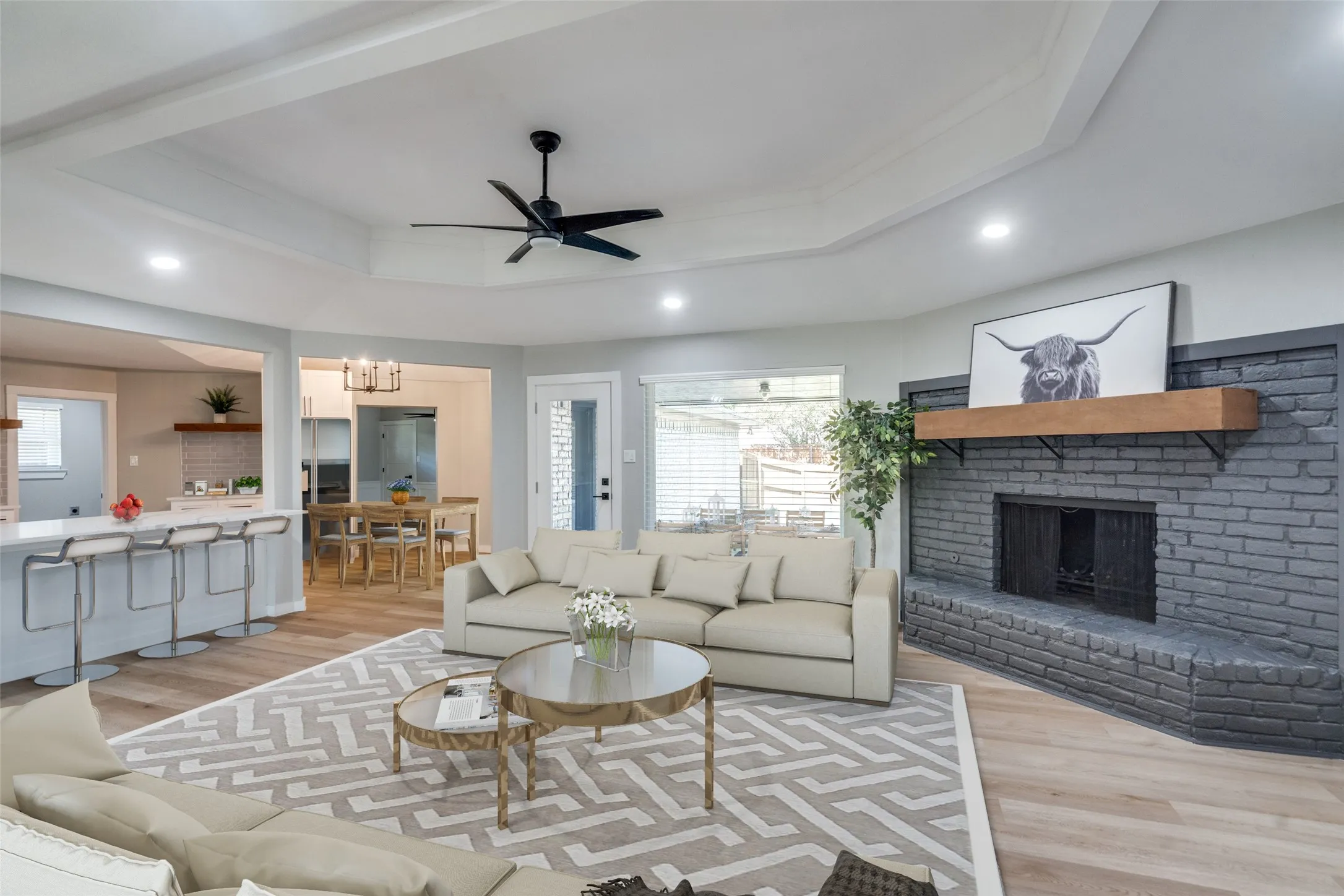 Living area with a raised ceiling, light wood-type flooring, a fireplace, recessed lighting, and ceiling fan