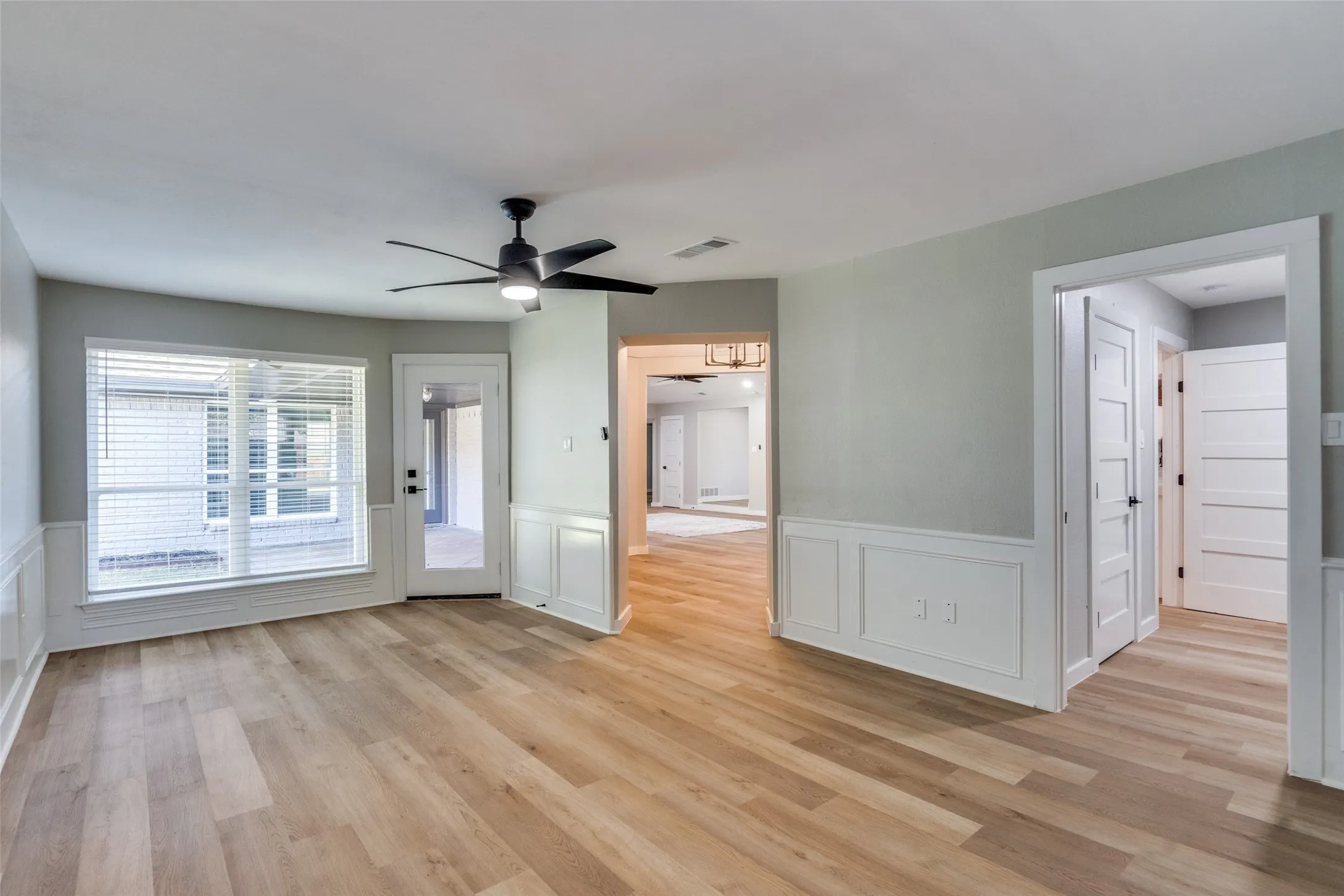 Unfurnished room with a ceiling fan, light wood-type flooring, a decorative wall, and a wainscoted wall