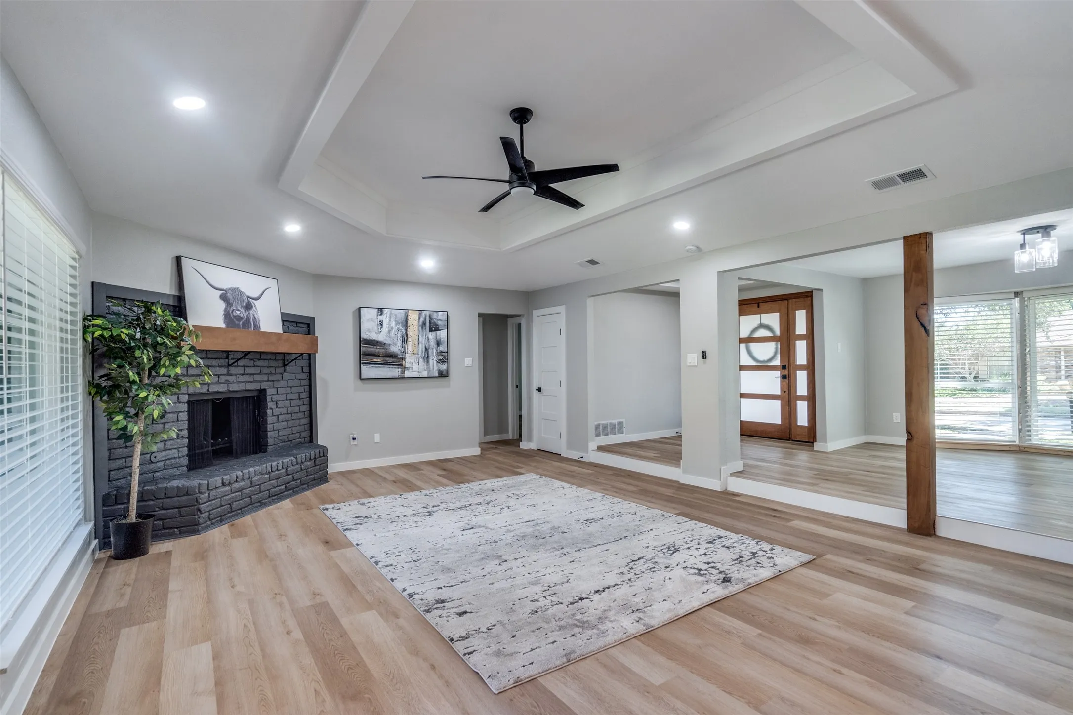 Living room with a raised ceiling, a ceiling fan, a fireplace, light wood finished floors, and recessed lighting