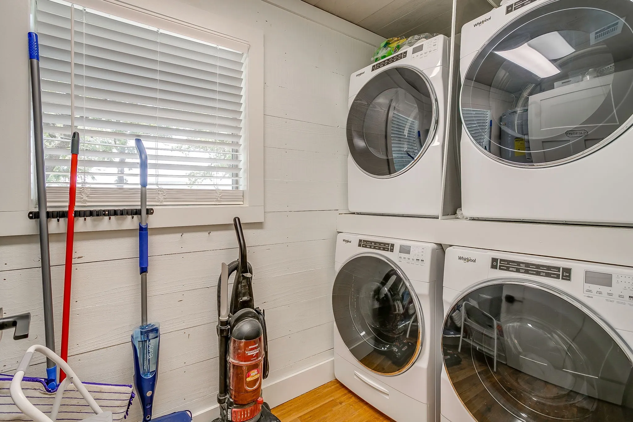 Washroom featuring stacked washing machine and dryer, light wood finished floors, and wooden walls