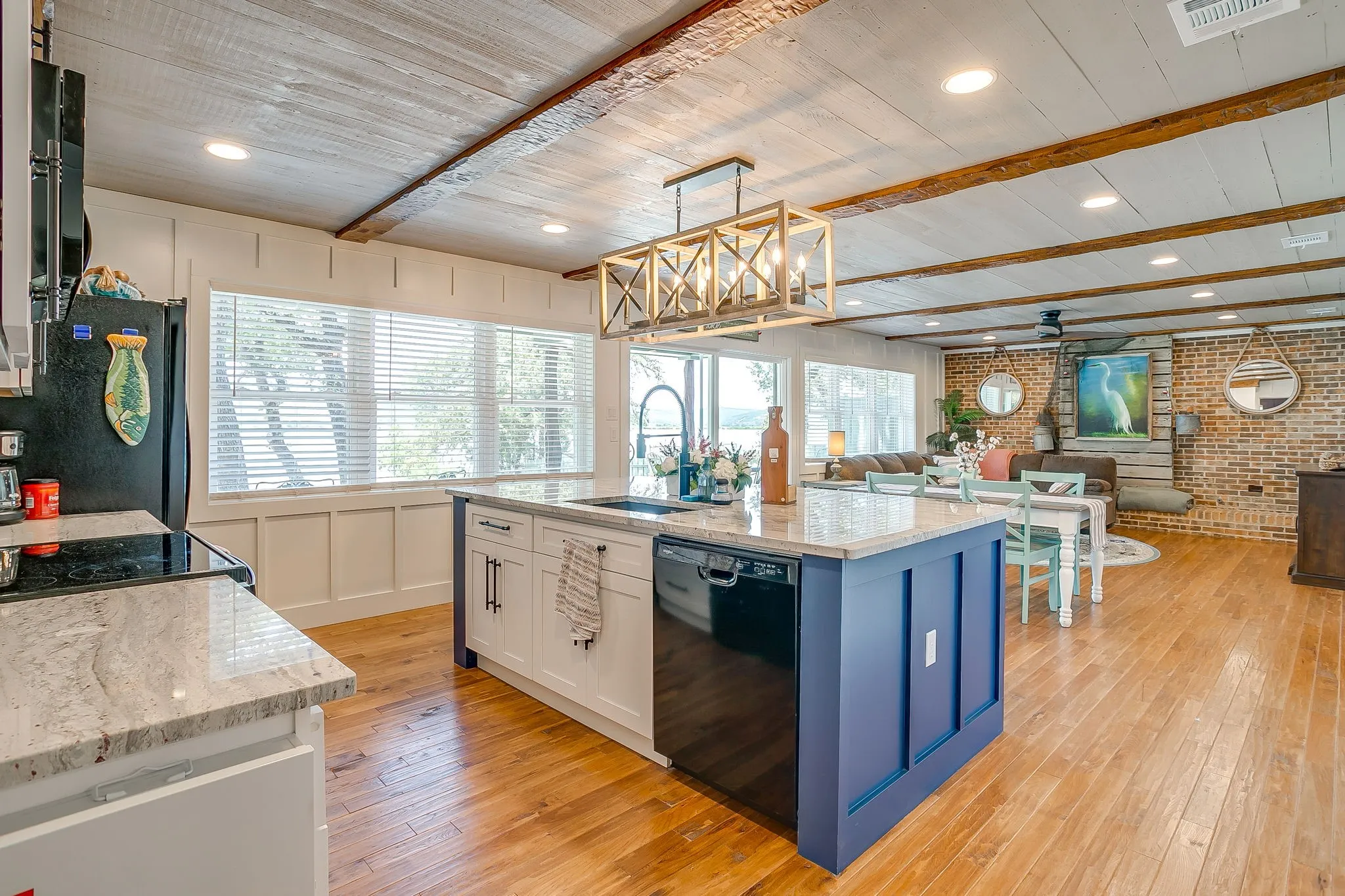 Kitchen featuring brick wall, light wood-style flooring, blue cabinets, black dishwasher, and open floor plan