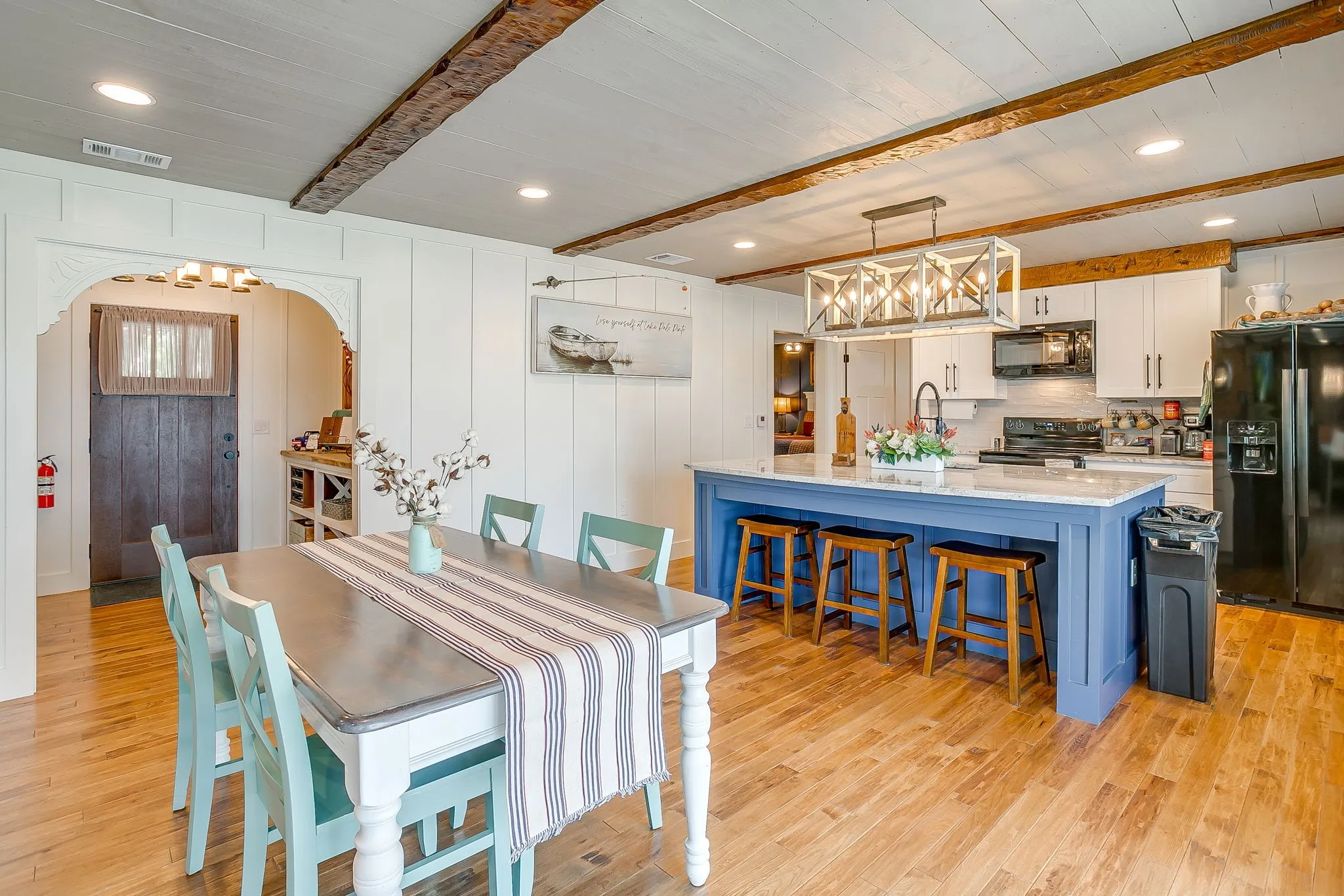 Dining area with a chandelier, beamed ceiling, light wood-style floors, recessed lighting, and arched walkways