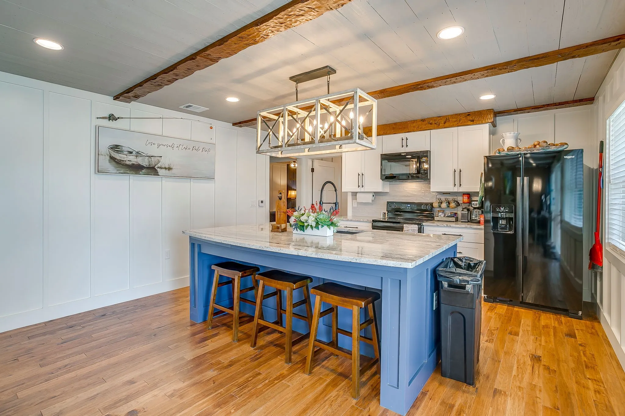 Kitchen with black appliances, beam ceiling, light wood finished floors, white cabinetry, and decorative backsplash