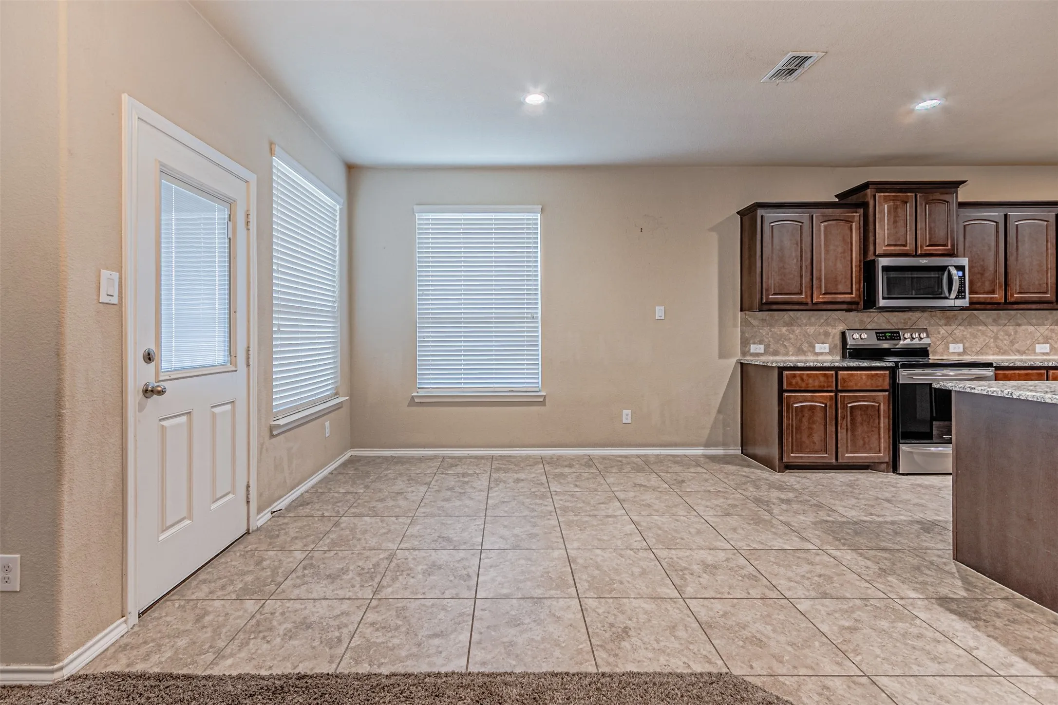Kitchen featuring stainless steel appliances, tasteful backsplash, light tile patterned flooring, dark brown cabinetry, and light stone counters