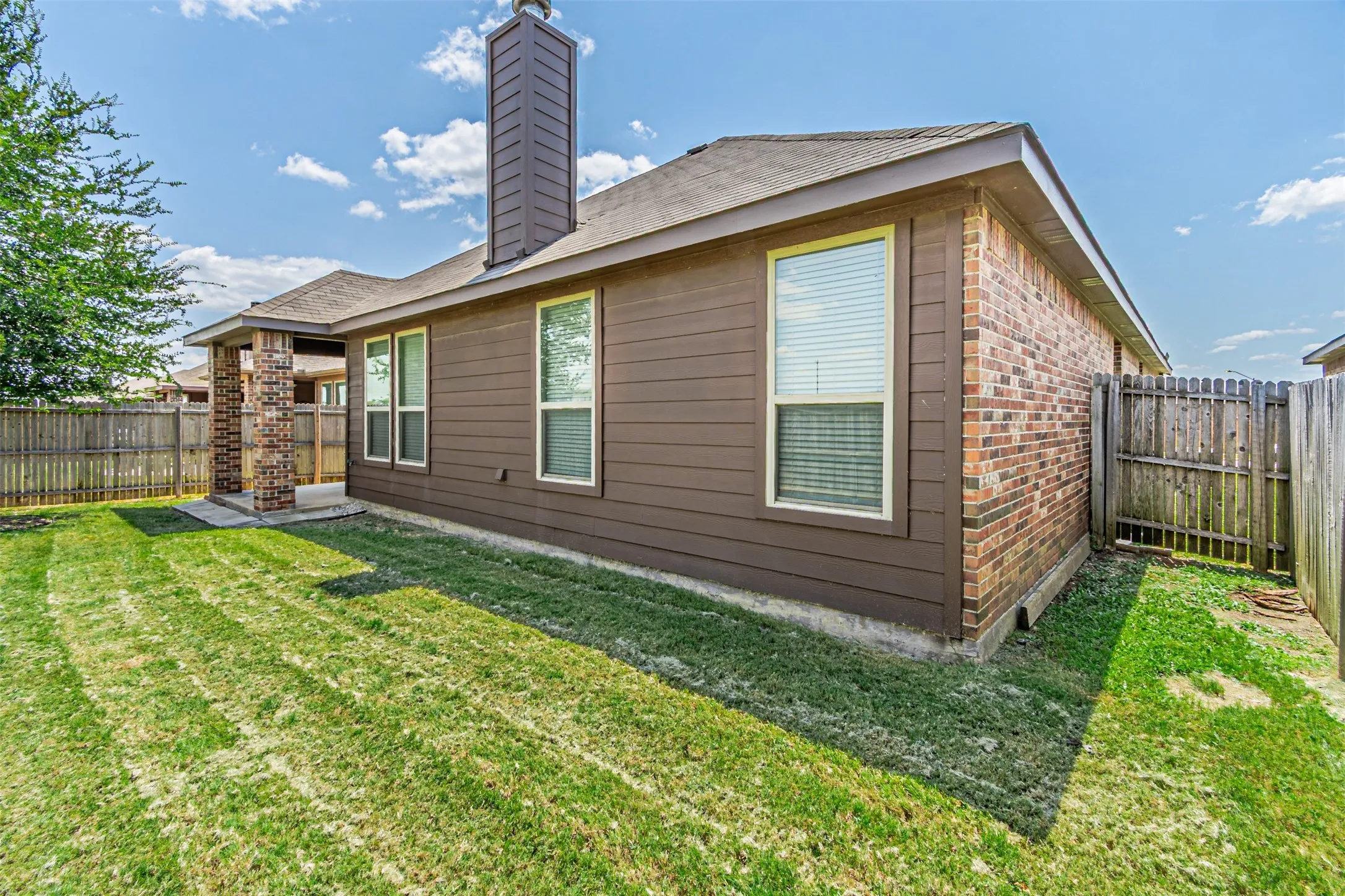 Back of house featuring a fenced backyard, a chimney, brick siding, and a shingled roof