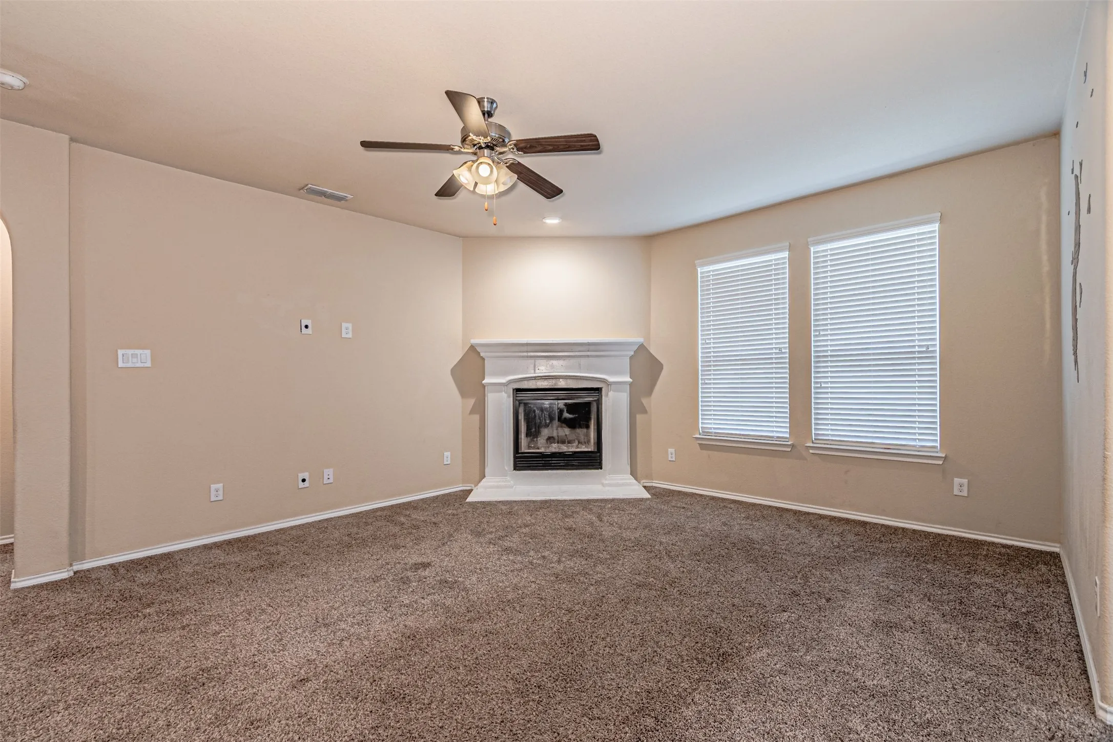 Unfurnished living room featuring a glass covered fireplace, carpet, ceiling fan, arched walkways, and recessed lighting