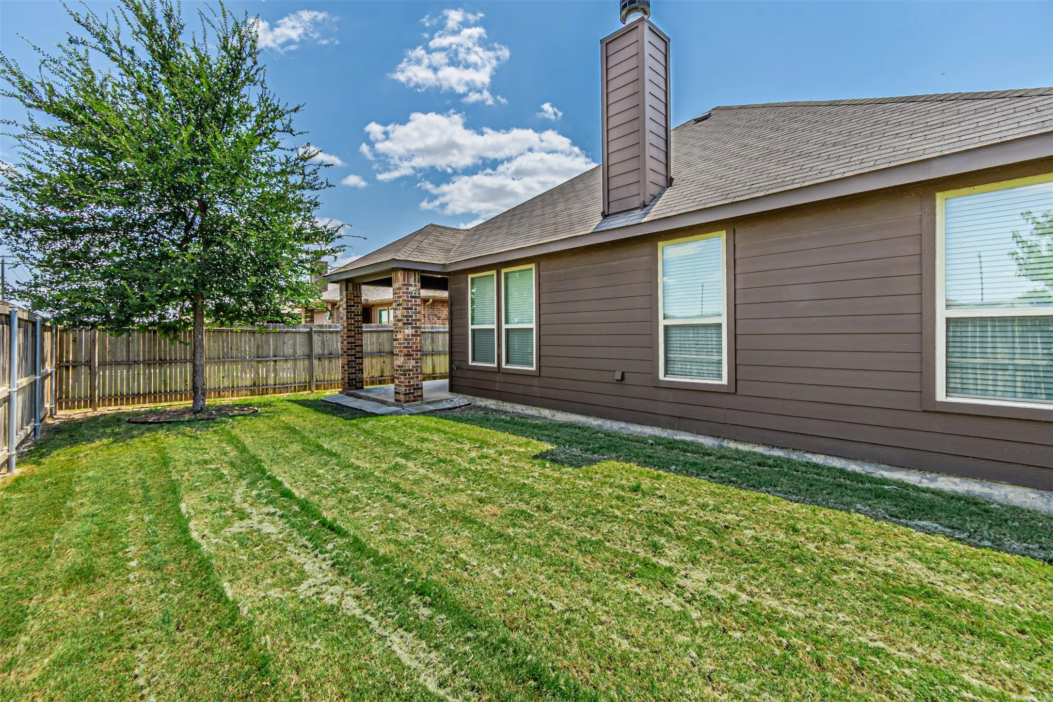 Back of house featuring a fenced backyard, a chimney, roof with shingles, and a patio area