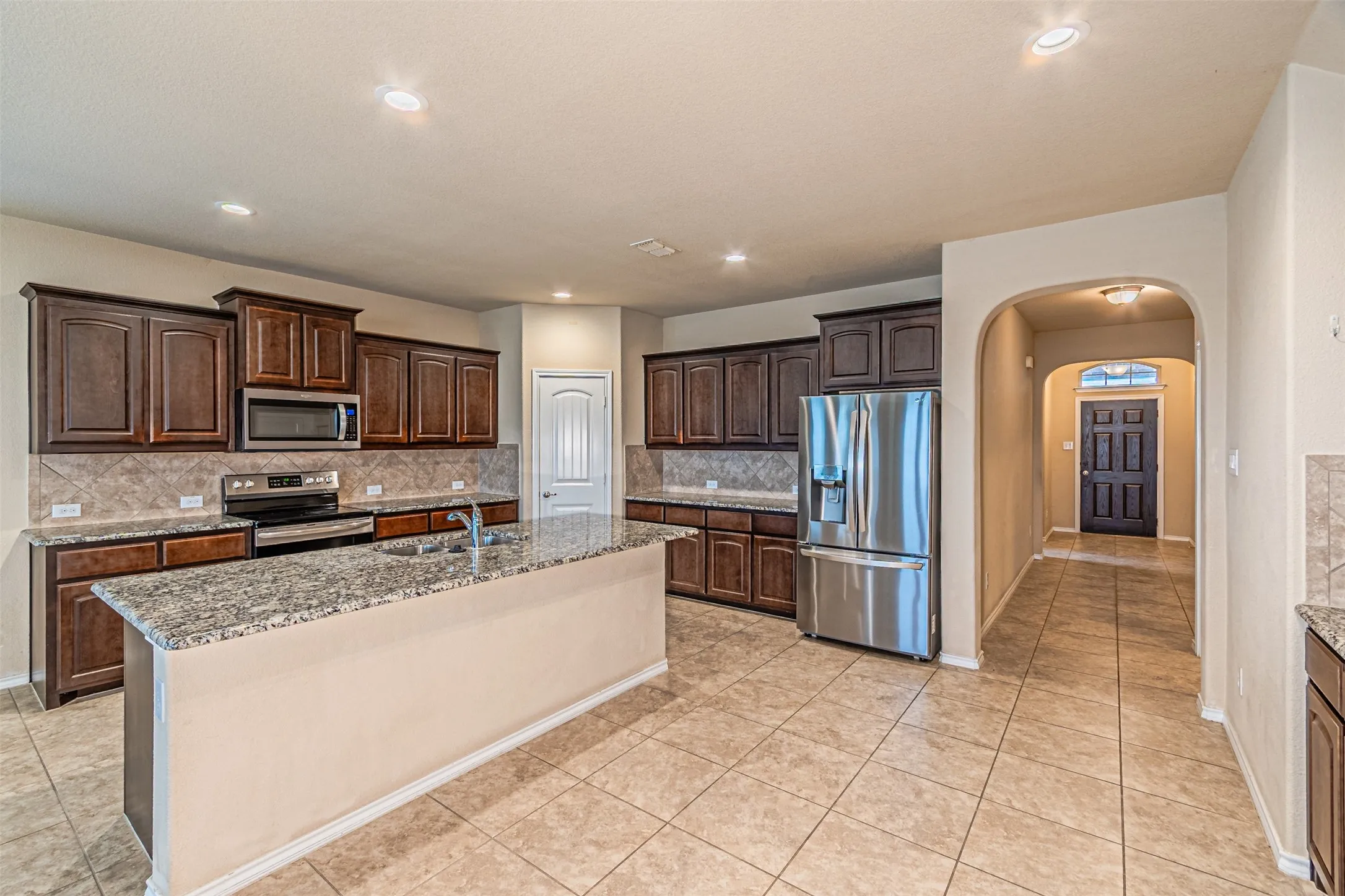 Kitchen featuring arched walkways, backsplash, appliances with stainless steel finishes, dark brown cabinetry, and light tile patterned floors