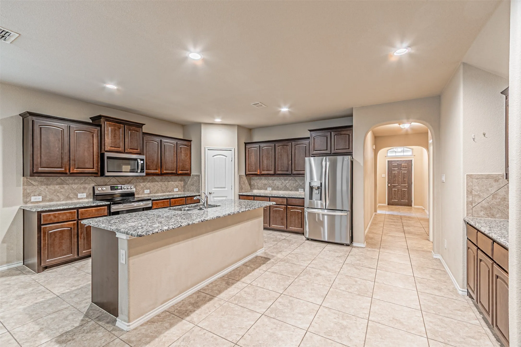 Kitchen featuring decorative backsplash, arched walkways, stainless steel appliances, dark brown cabinetry, and light stone countertops