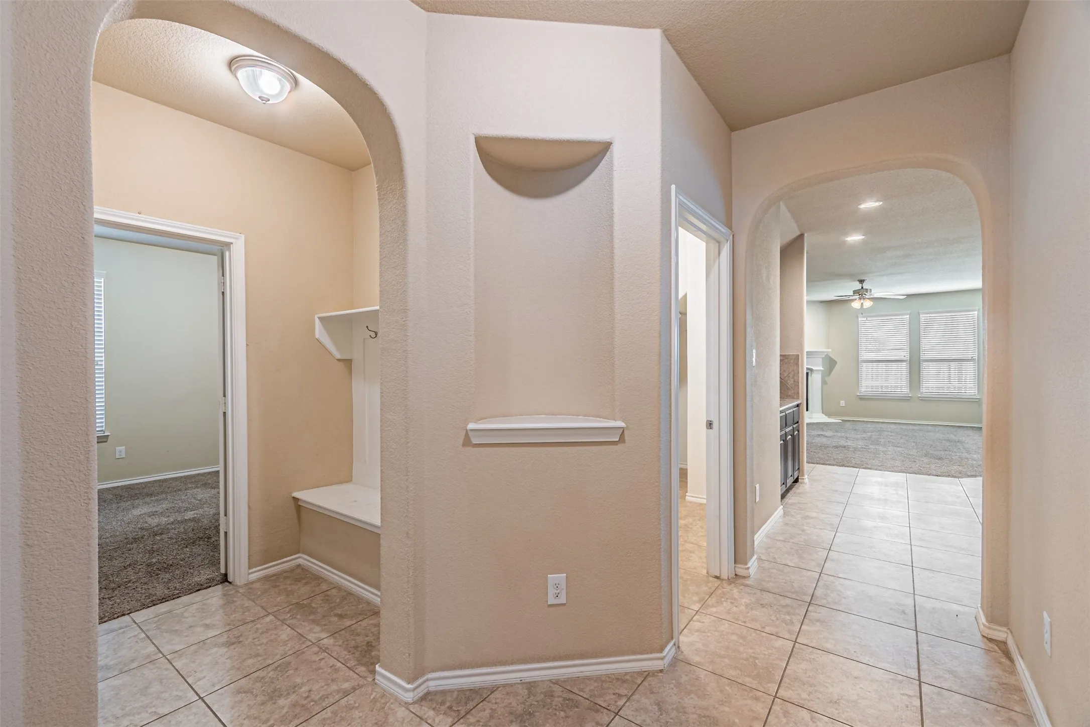 Hallway featuring arched walkways, light tile patterned floors, light carpet, and a textured ceiling