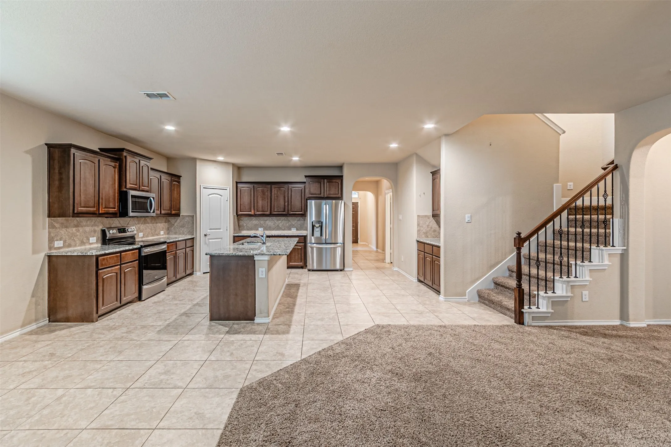Kitchen with arched walkways, light tile patterned floors, stainless steel appliances, decorative backsplash, and a kitchen island with sink