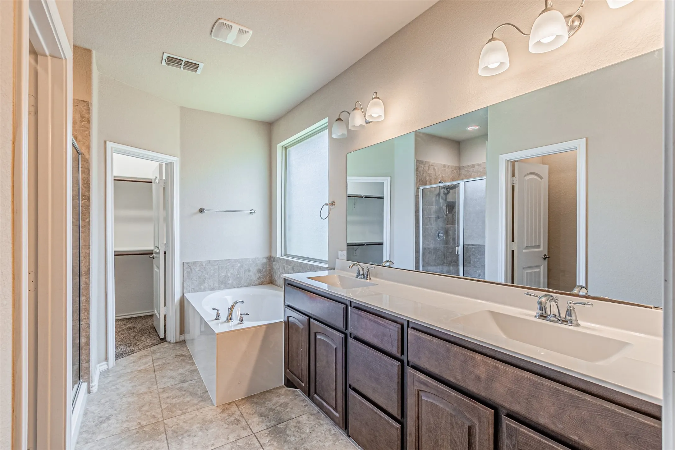 Full bath featuring a spacious closet, a stall shower, double vanity, a bath, and tile patterned floors