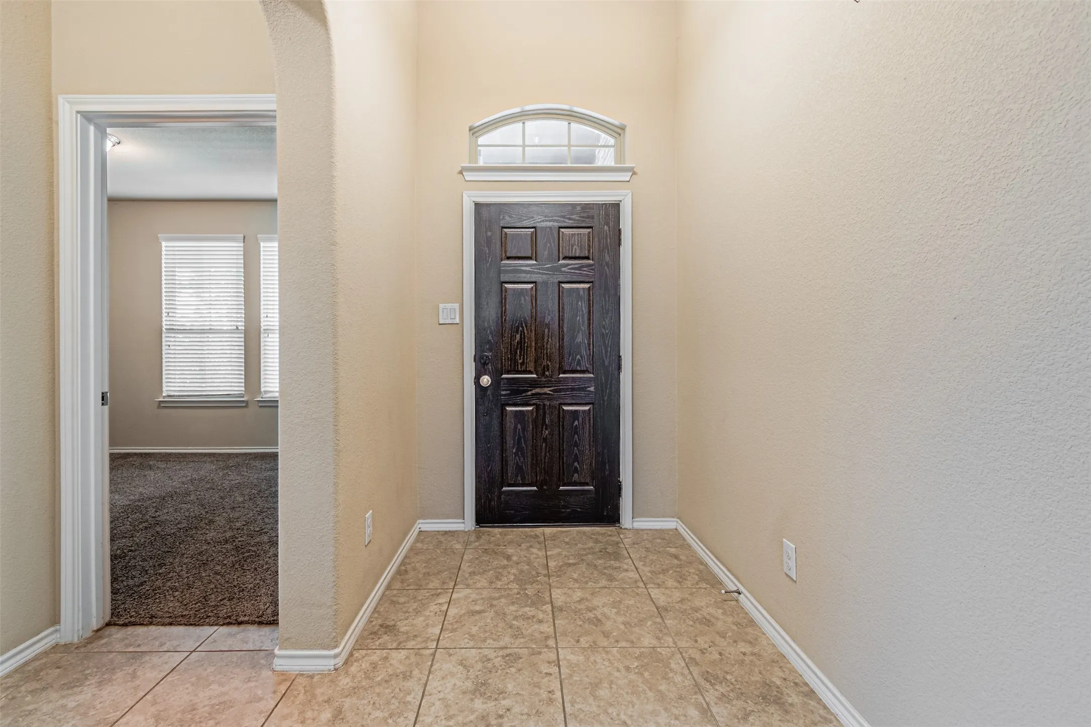 Foyer with plenty of natural light, light tile patterned floors, arched walkways, and light carpet