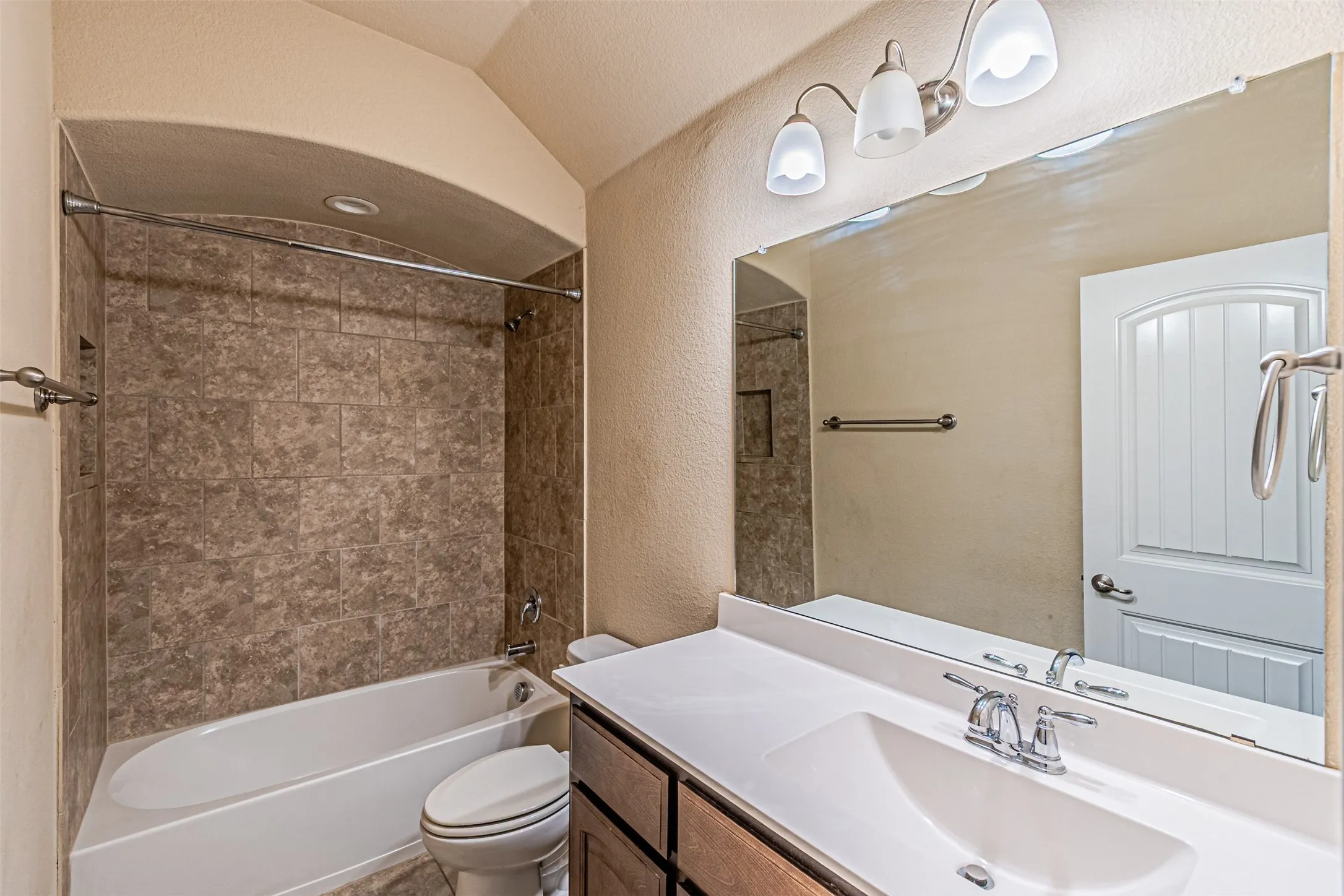 Bathroom featuring a textured wall, vanity, shower / bathtub combination, and vaulted ceiling