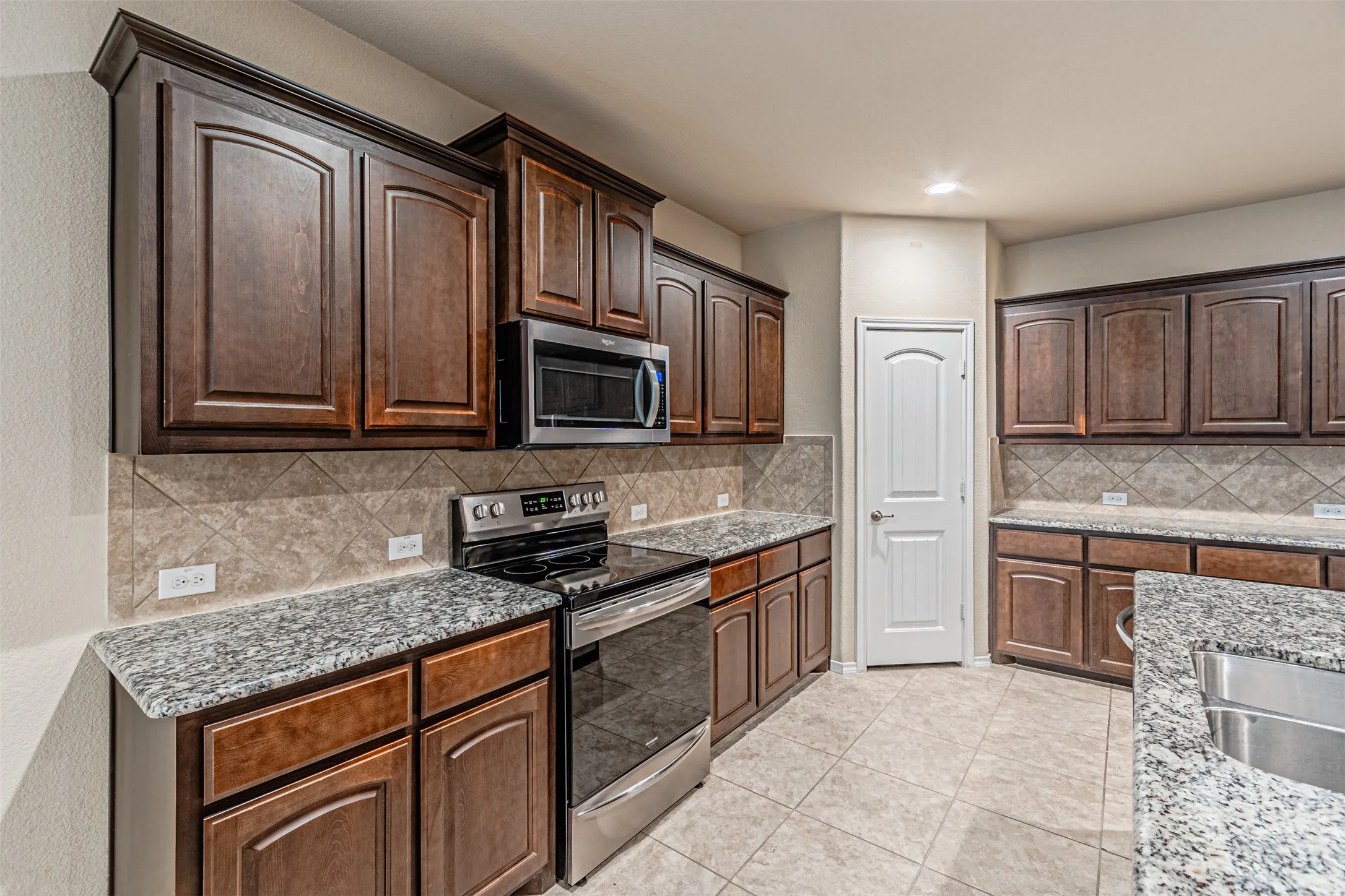 Kitchen with appliances with stainless steel finishes, light tile patterned floors, light stone counters, decorative backsplash, and recessed lighting