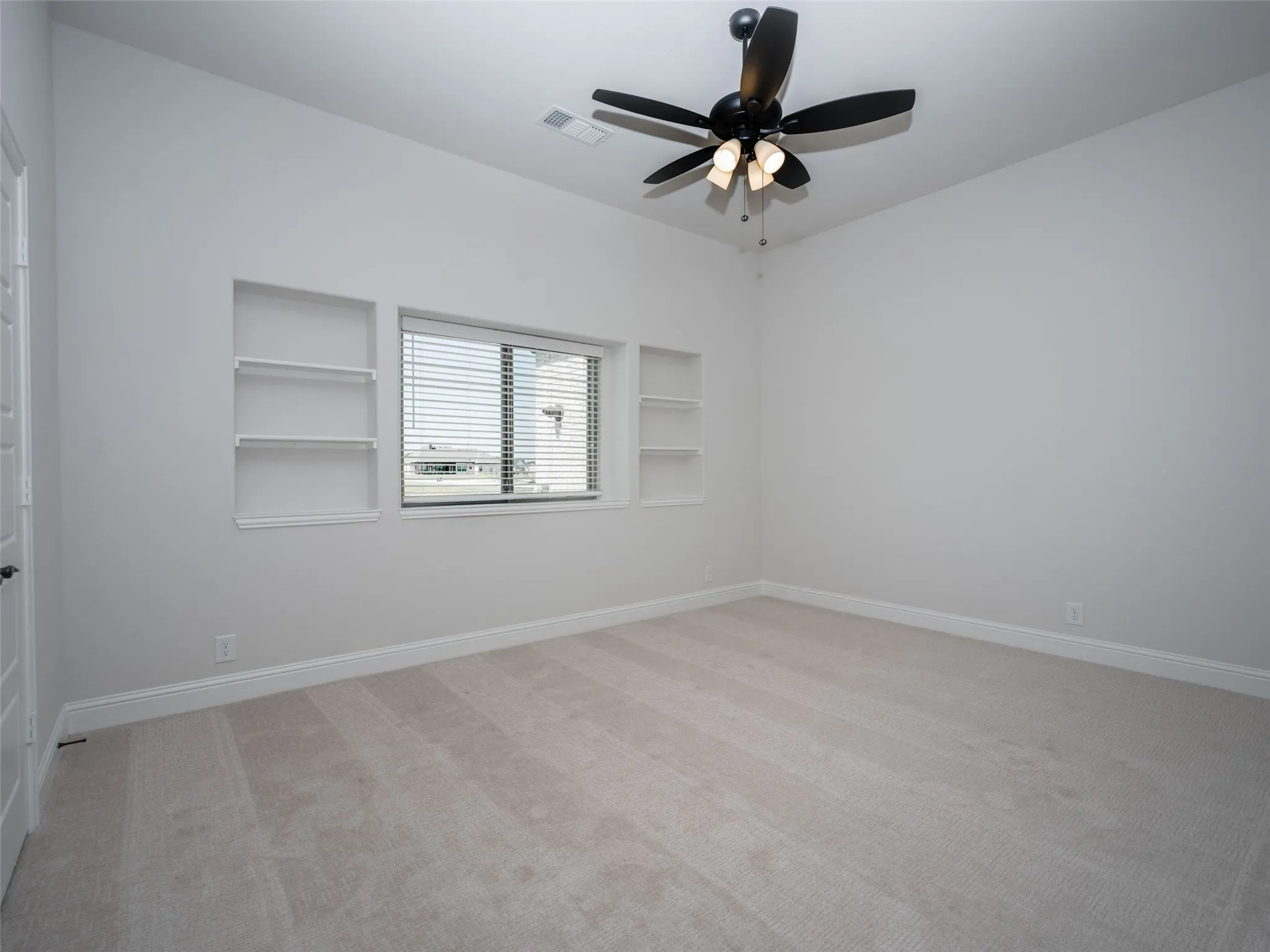 Empty room with built in shelves, light carpet, and a ceiling fan