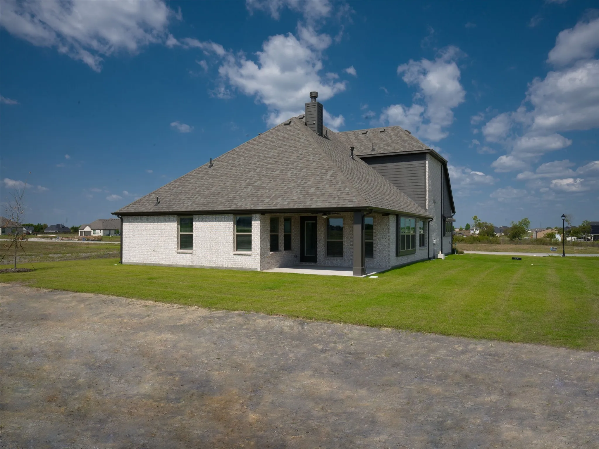 Back of house with brick siding, a shingled roof, a lawn, and a patio area
