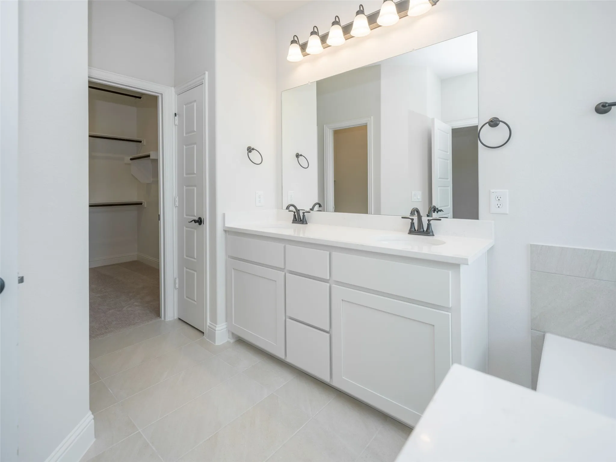 Full bath with double vanity, light tile patterned flooring, and a spacious closet