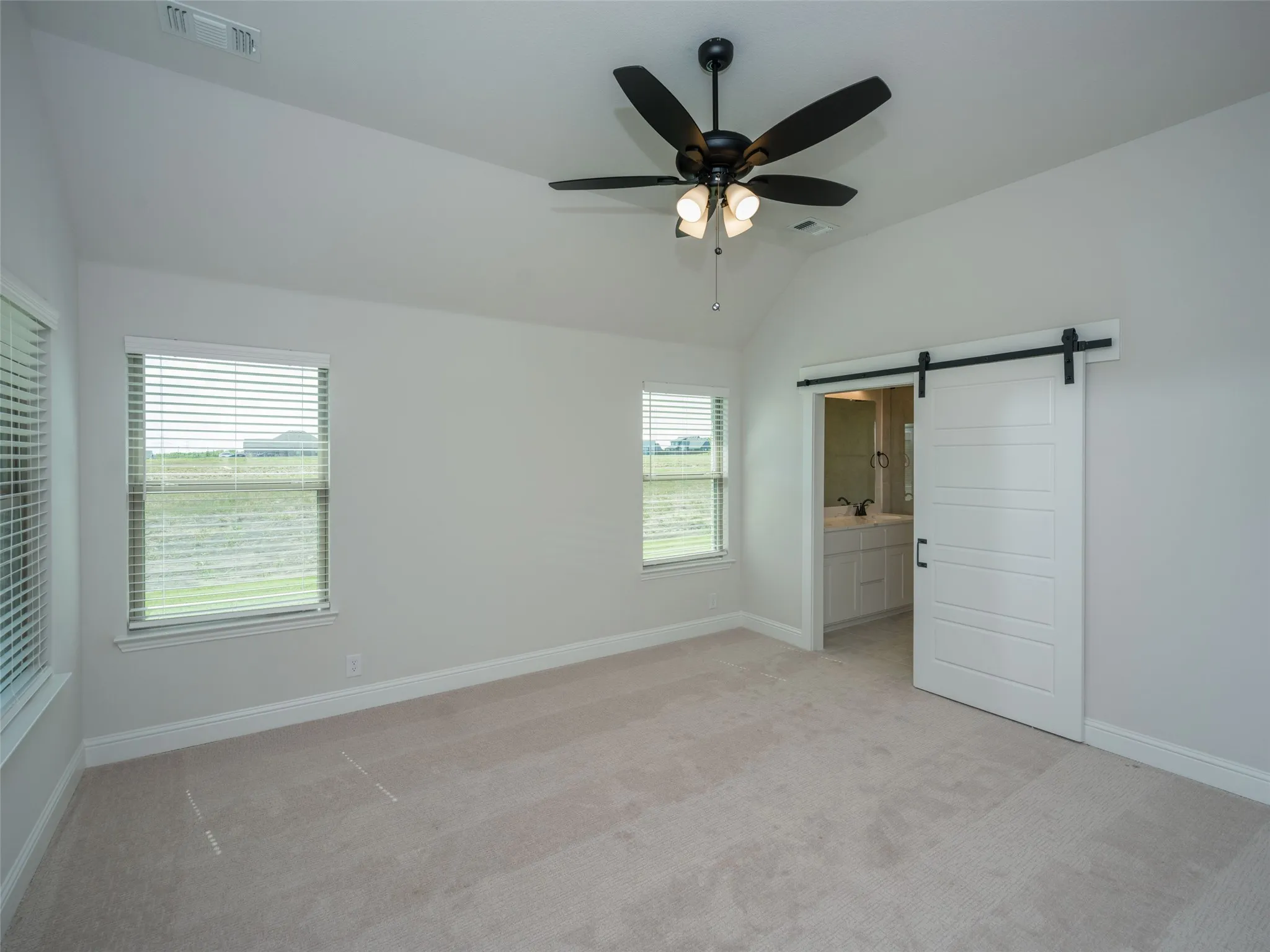 Unfurnished bedroom featuring a barn door, lofted ceiling, light colored carpet, ensuite bathroom, and ceiling fan