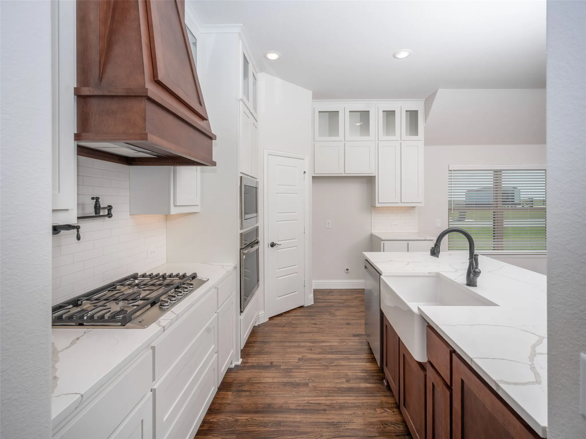 Kitchen with tasteful backsplash, white cabinetry, light stone counters, dark wood-type flooring, and appliances with stainless steel finishes