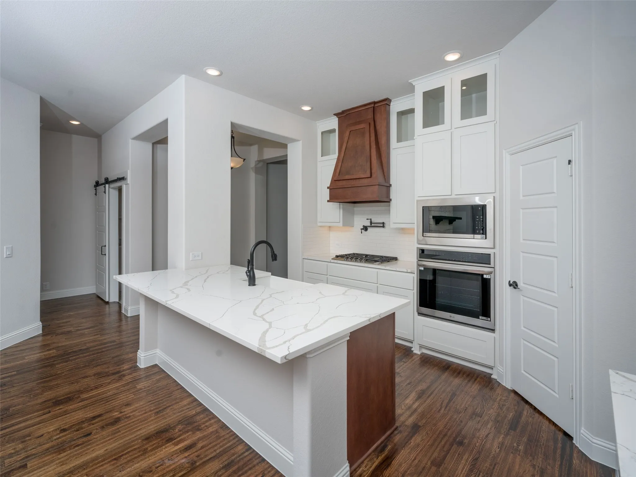 Kitchen featuring a barn door, light stone counters, tasteful backsplash, appliances with stainless steel finishes, and glass insert cabinets